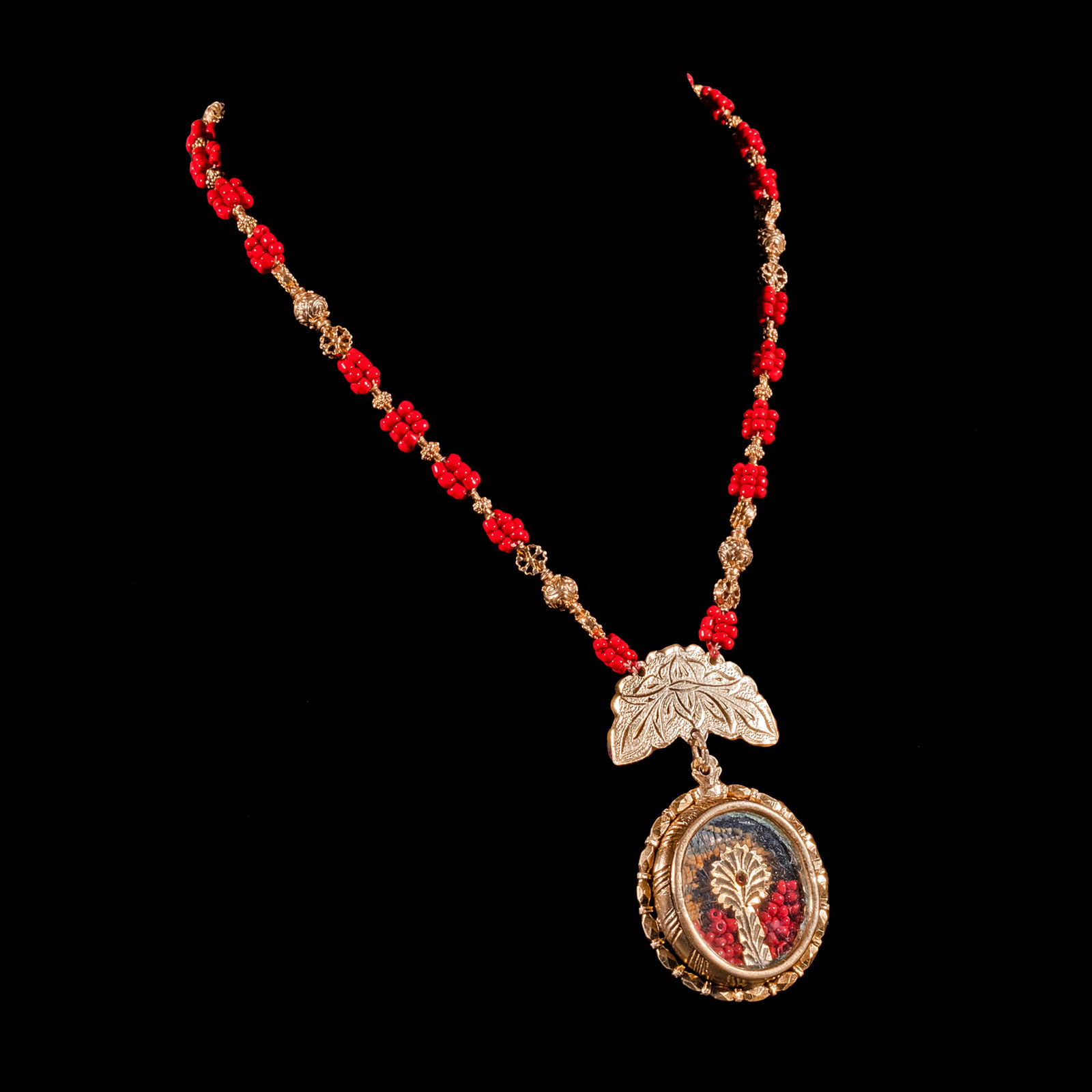 A Tamburin Coral Necklace: Set in silver and dipped in yellow gold, theTamburin necklace features intricately designedfiligree beads stationed between coral beadclusters. A reliquiario suspends from thenecklace encasing coral b