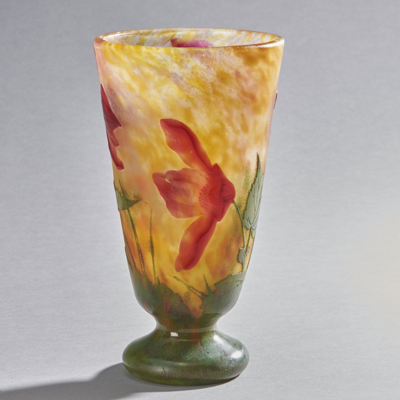 Daum Nancy Footed Cameo Glass Vase: A circa 1900 French hand blown cameo glass vase by Daum Nancy. The vase has a cylindrical form tapering to a round footed base decorated with leaves and red flowers in cameo relief. Signed Daum Nancy