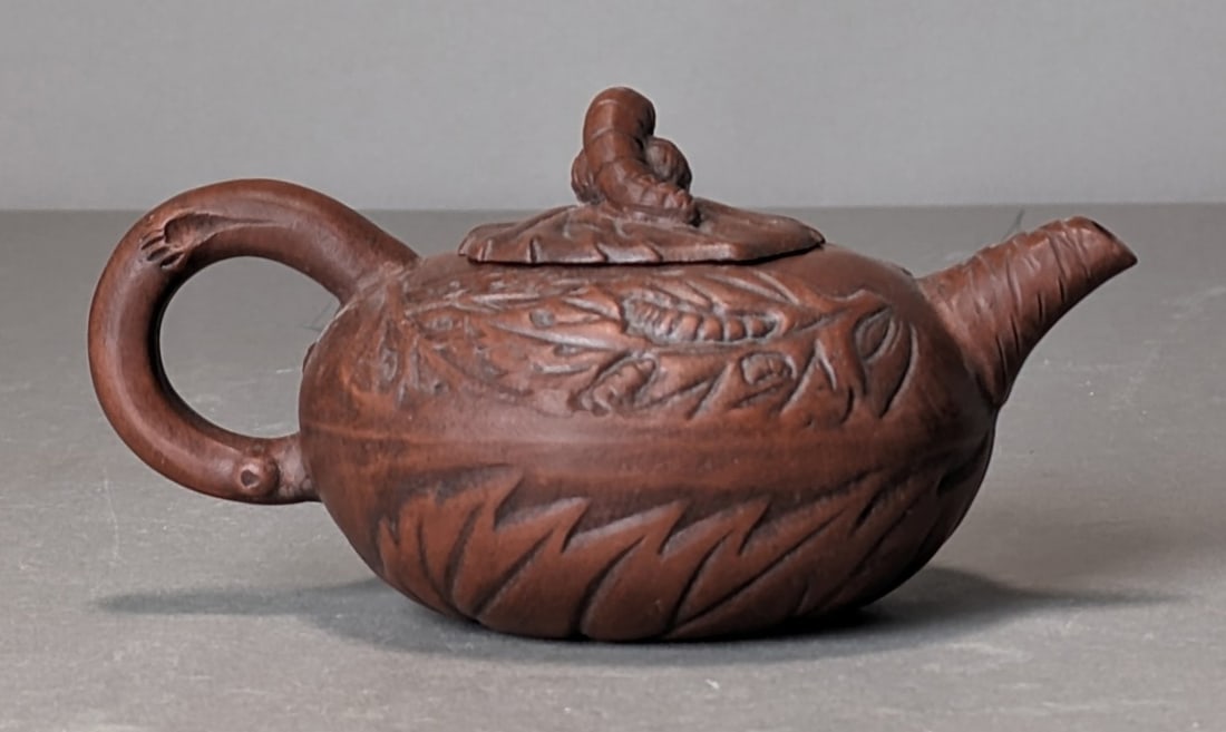 Chinese Zisha Teapot with Foliate Decoration: Chinese Zisha teapot with foliate decoration and sculpted lid; mark on underside. Dimensions: Height: 3.5 in. Width: 6.5 in. Depth: 4.5 in.