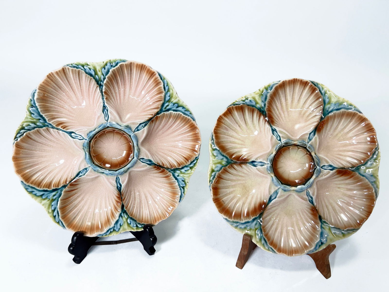 Pair of Sarreguemines Majolica Oyster Plates: A pair of antique French Majolica oyster plates, each featuring a six-well floral shell design surrounding a central sauce well. Produced by Sarreguemines, a renowned French ceramics manufacturer know