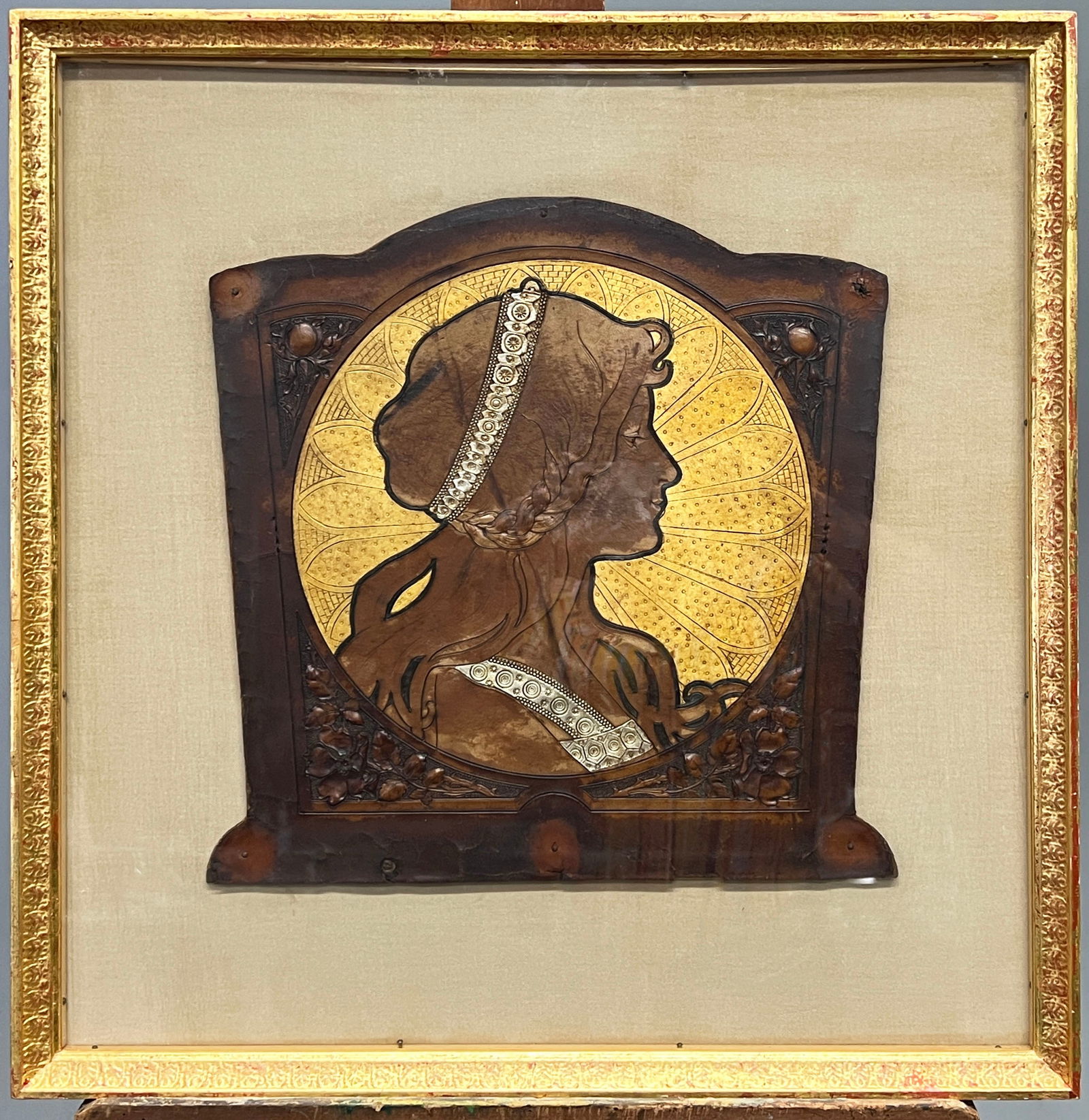 D'après Alphonse Mucha, Leather Work: D'après Alphonse Mucha (1860-1939), framed leather work panel Dimensions: 12.5" x 12.5" (sight); 19.75'' x 19.5'' (framed) Weight: 119 ounces