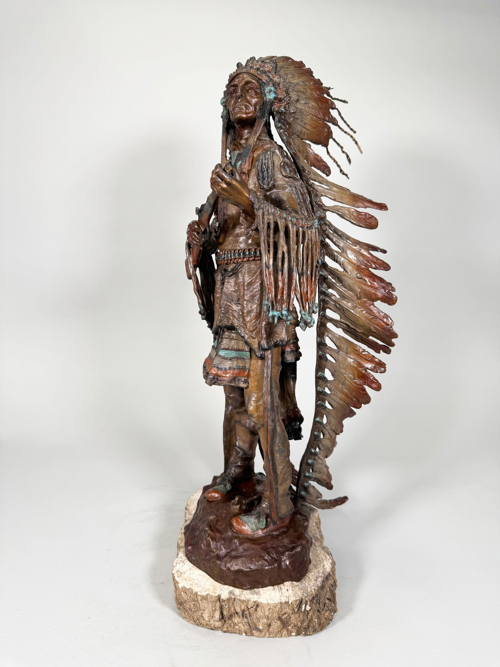 Carl Kauba Bronze Sculpture: Carl Kauba (1865 - 1922 Austria, USA) Cold painted bronze sculpture of a Native American chief with a rifle mounted on a stone base in the form of a tree trunk. Tip of rifle is missing. Signed on bron