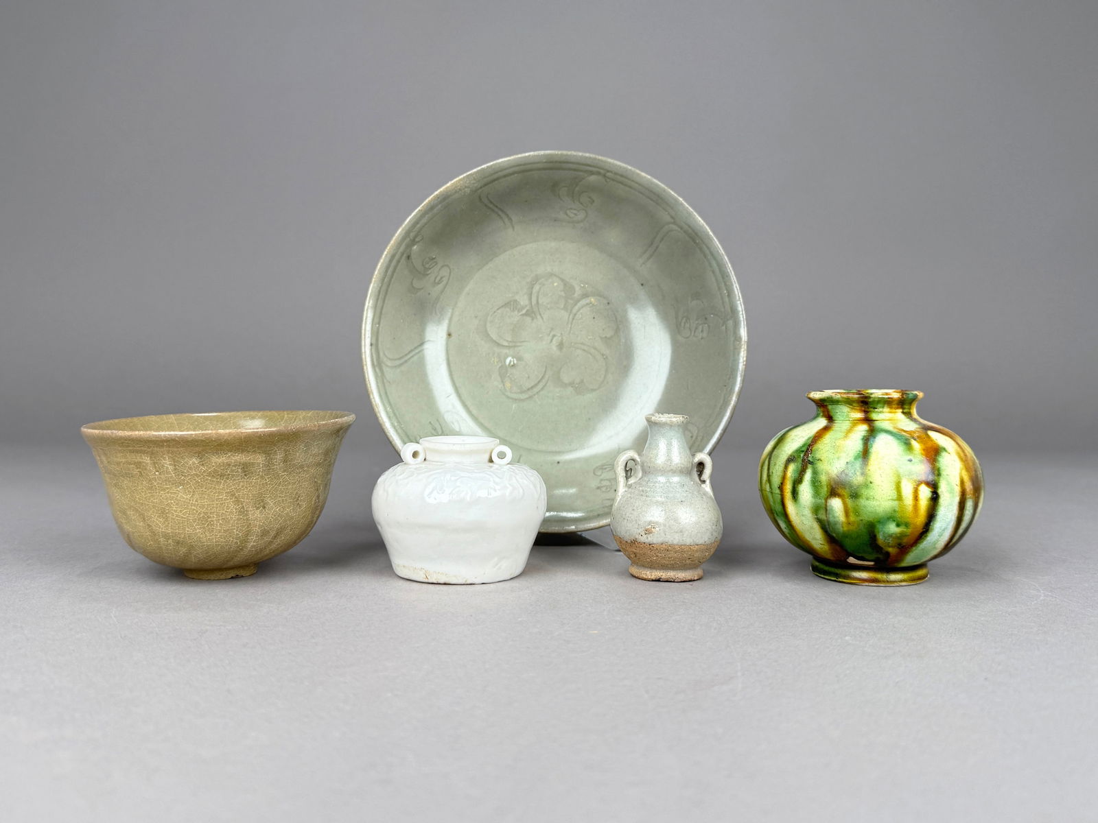 Group of Five Asian Ceramic Items: A group of five Asian ceramics including a flared rim celadon cup, celadon floral plate, Blanc de Chine jar with small ring handles, double gourd vase with handles, and a sancai glazed flared rim