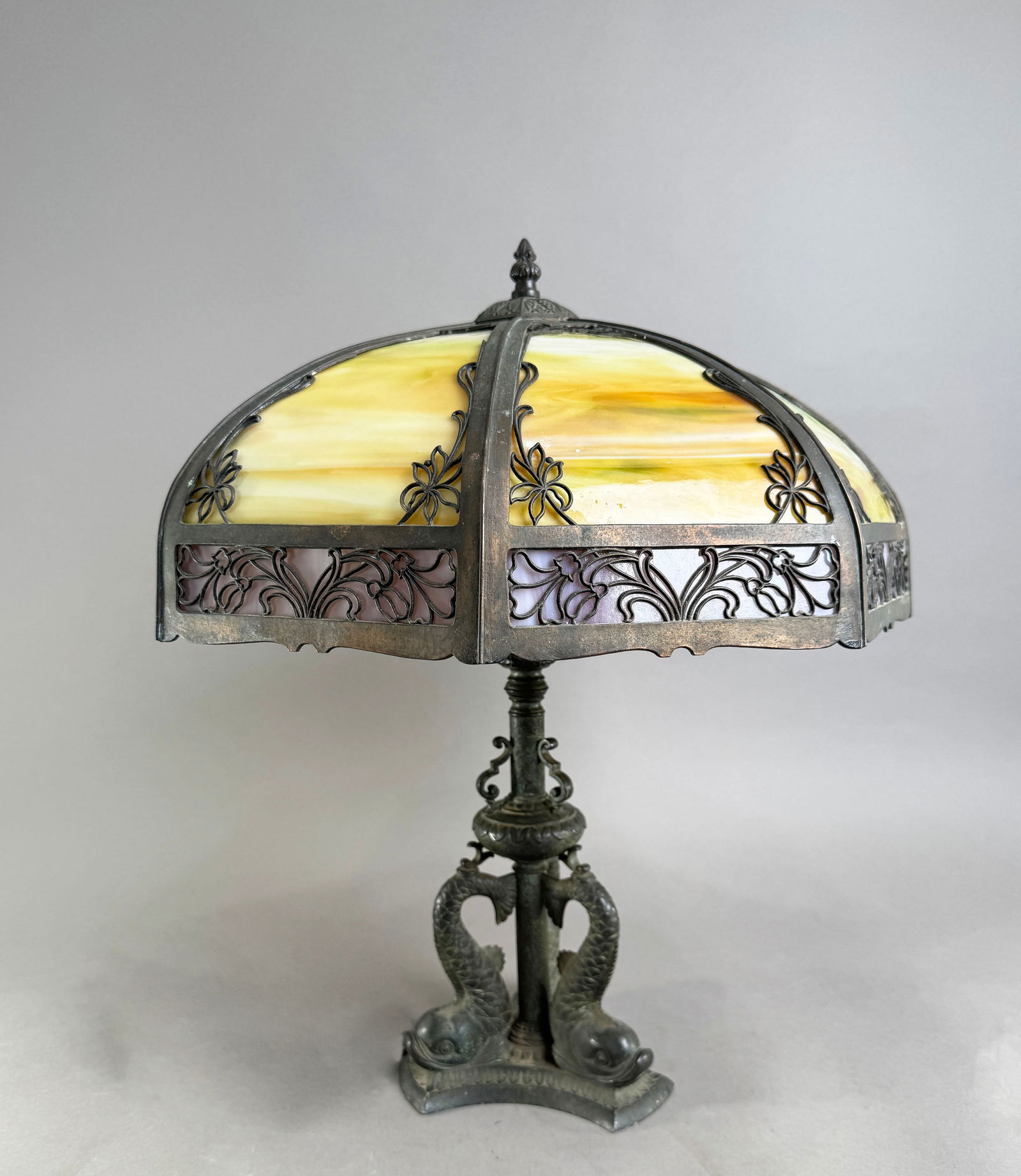 Stained Glass Table Lamp with Bronze Dolphin Base: Pairpoint Dolphin table lamp with Edward Miller & Co. slag glass lamp shade. Base is lacquered bronze, as indicated by sticker on base. 20.75" x 17.2" 202 oz.
