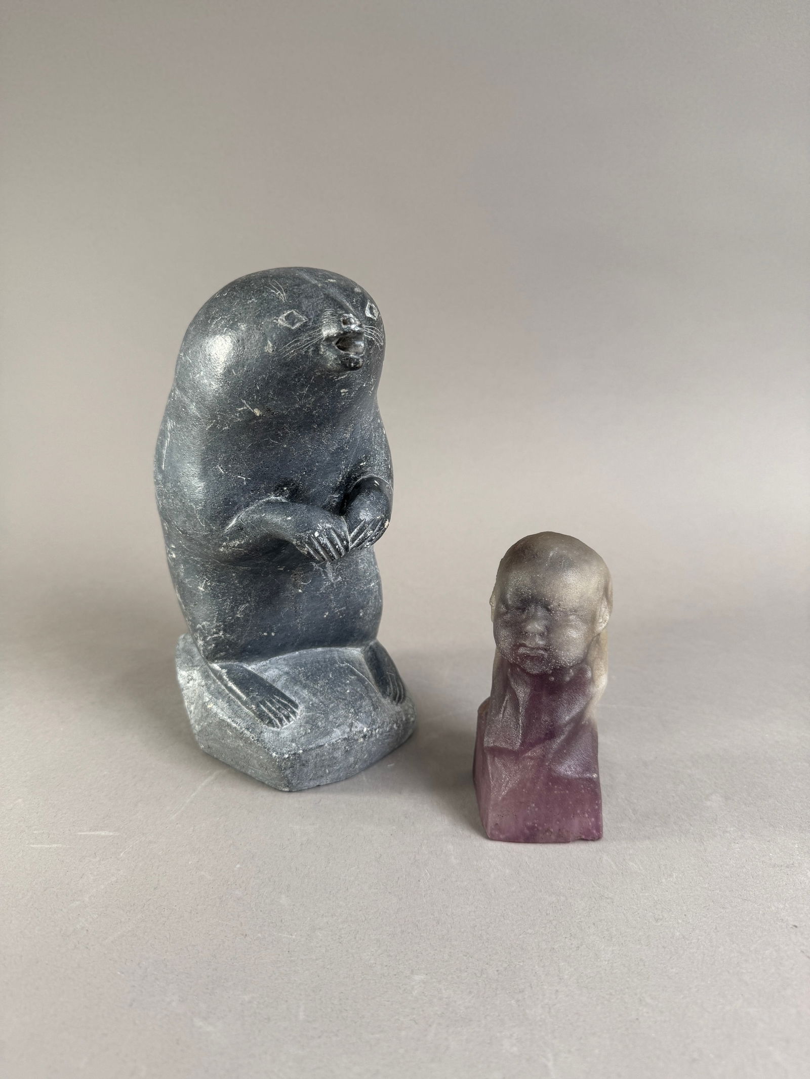 Two Inuit Carvings: Seal and Head: Two Inuit carvings. One is a grey stone carving of a seal, 8.5'' tall. The other is a smaller, 4.25'' tall carving of a head in purple stone. Total weight: 193 oz.
