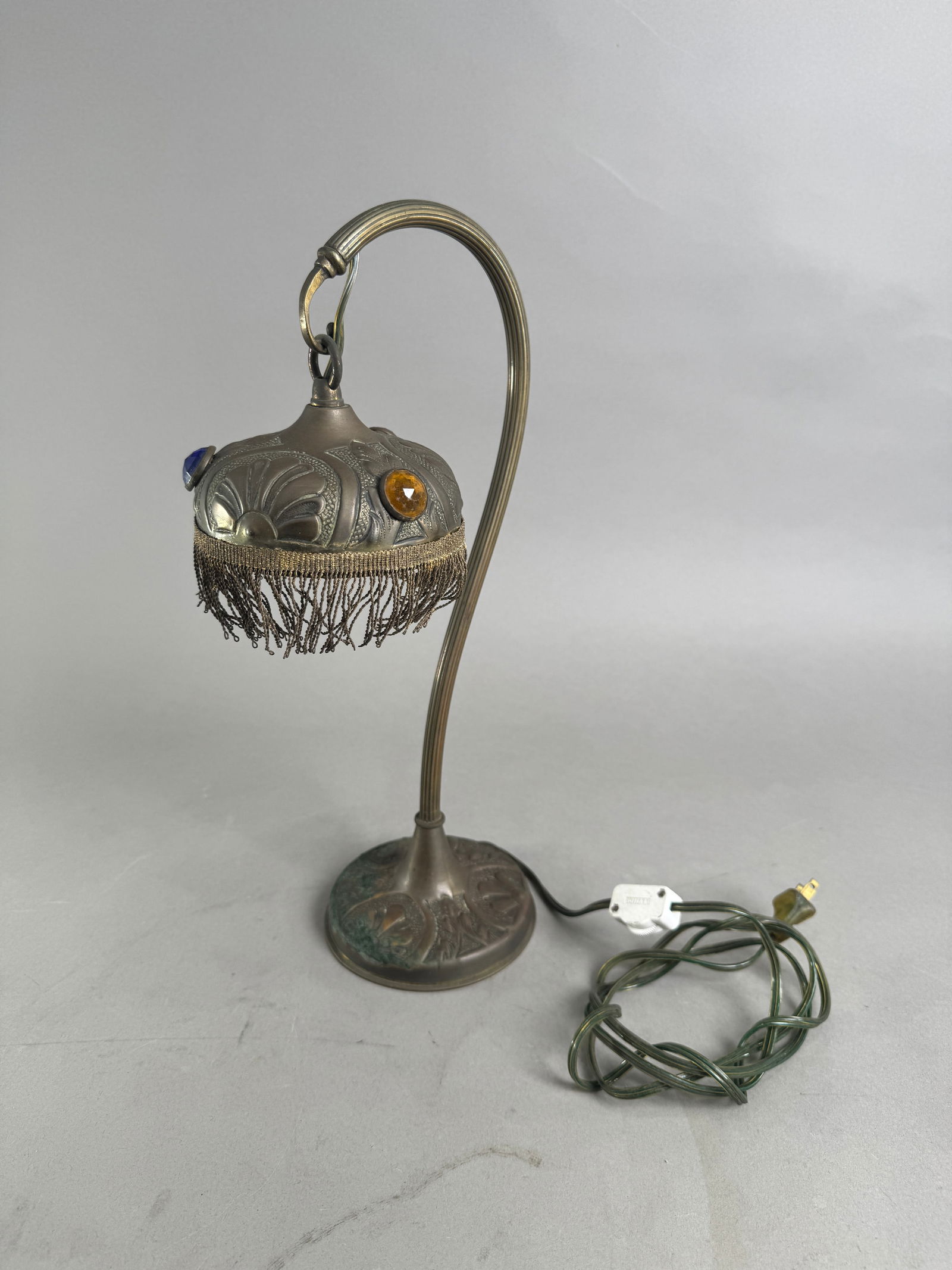 Vintage Brass Table Lamp with Fringed Shade: Vintage brass table lamp featuring a gooseneck design and a fringed shade adorned with plastic jewels. Measures 15.5" in height and weighs 44 oz. Decorative floral design on base.