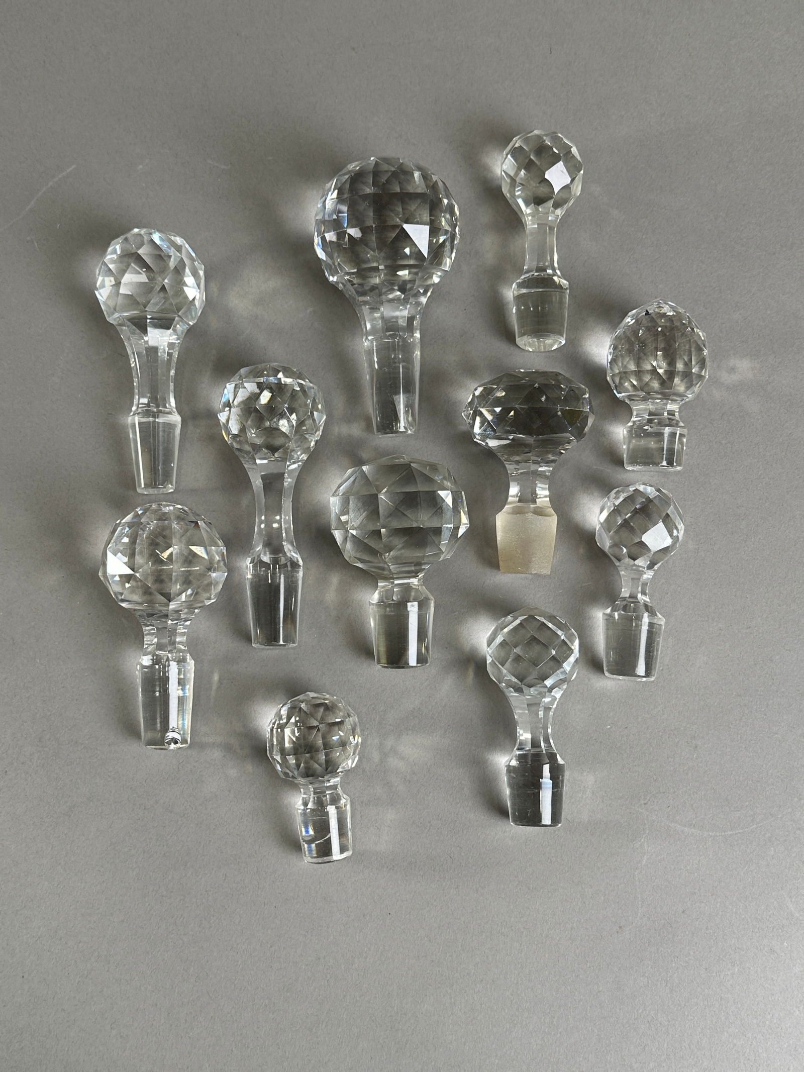 Collection of Crystal Glass Bottle Stoppers: Collection of crystal glass bottle stoppers. The stoppers vary in size from 2.5 to 5 inches long and weigh 97 oz. Faceted spherical and geometric designs.