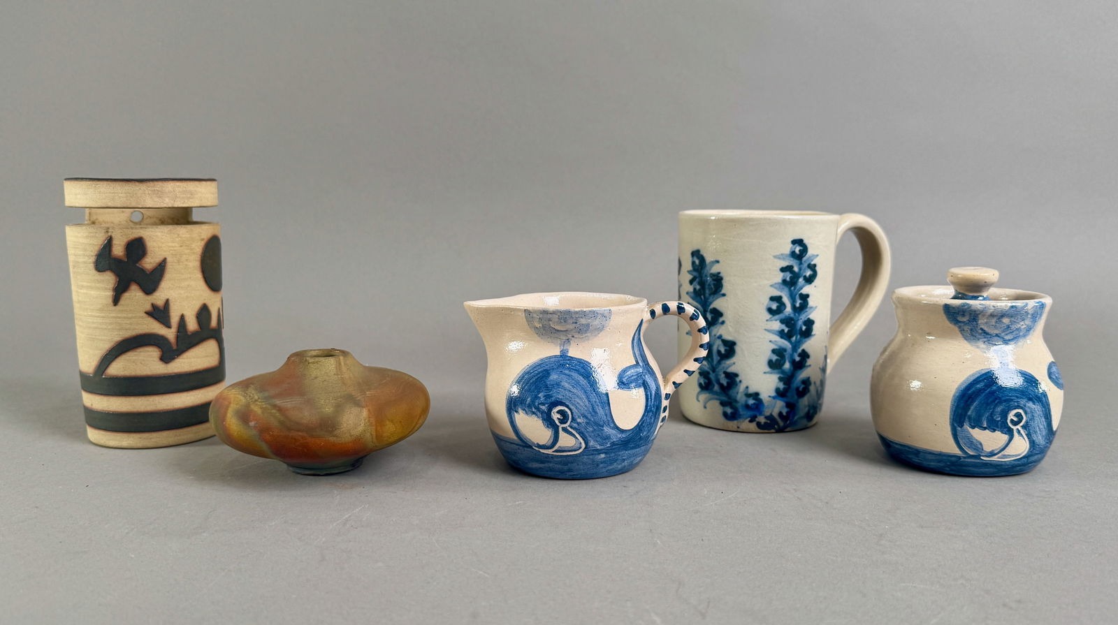 Five Piece Assorted Studio Pottery Group: Five piece group of studio pottery. Includes a cylindrical vase, a small iridescent bowl, a small whale motif pitcher, a floral motif mug, and a whale motif lidded jar. All pieces signed on bottom. Ta