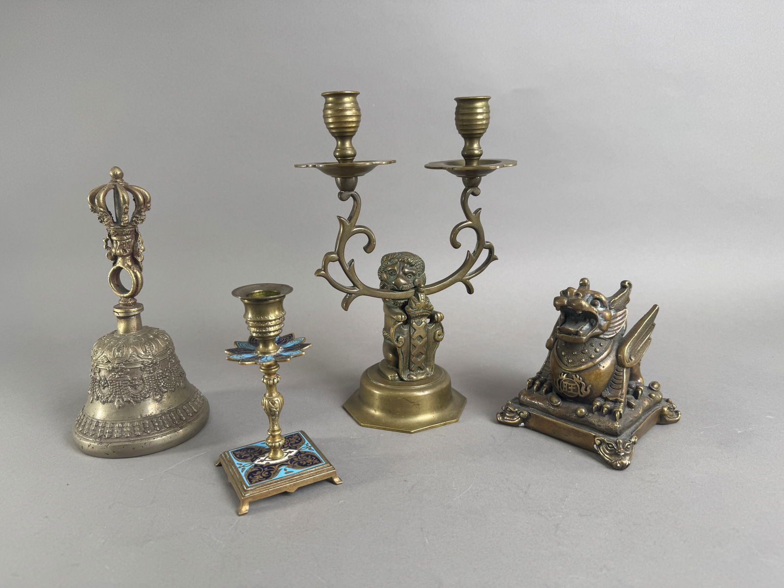 Collection of Metal Decorative Items: Bell, Candelabras, Figurine: A collection of decorative metal items including a bell with ornate handle, two candelabras (one double arm with a figure), and a winged dragon figurine. Sizes range from 5.5 to 10.75 inches tall. Tot