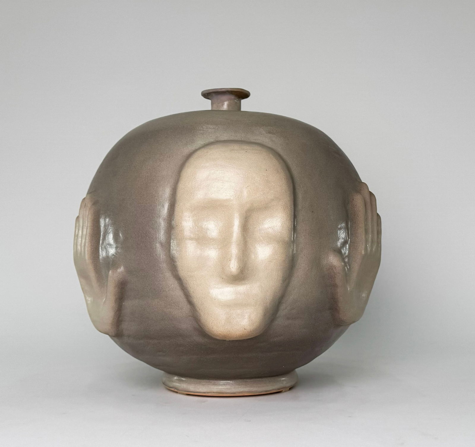 Loran Pottery Vessel with Face and Hands, #1045: A Loran pottery vessel featuring a face on one side and hands on the other. Marked #1045 on the base. Dimensions: 13.5"H x 13"D. Weight: 175 oz.