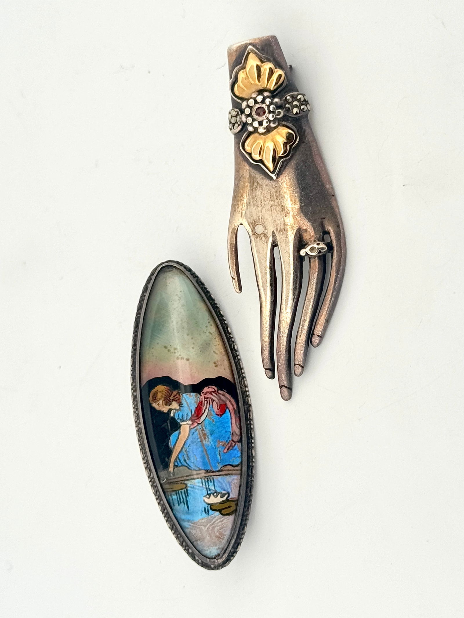 Two Sterling Silver Brooches: Two vintage sterling silver pins. One is an oval pin with a butterfly wing scene, marked 'England Sterling'. The other is a hand-shaped pin with gold-tone accents, marked '825 18K'.