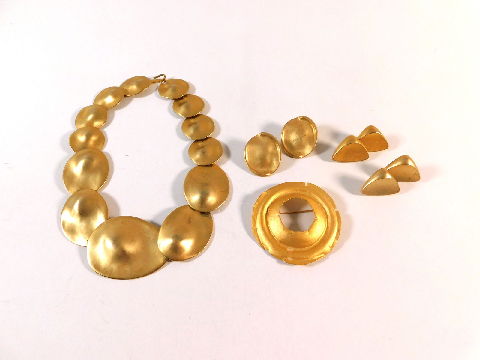 Gold Tone Jewelry Group: A gold-tone costume jewelry set featuring a necklace with large oval links, a circular brooch, and two pairs of earrings. The necklace measures approximately 18 inches. Total weight is 194.4g