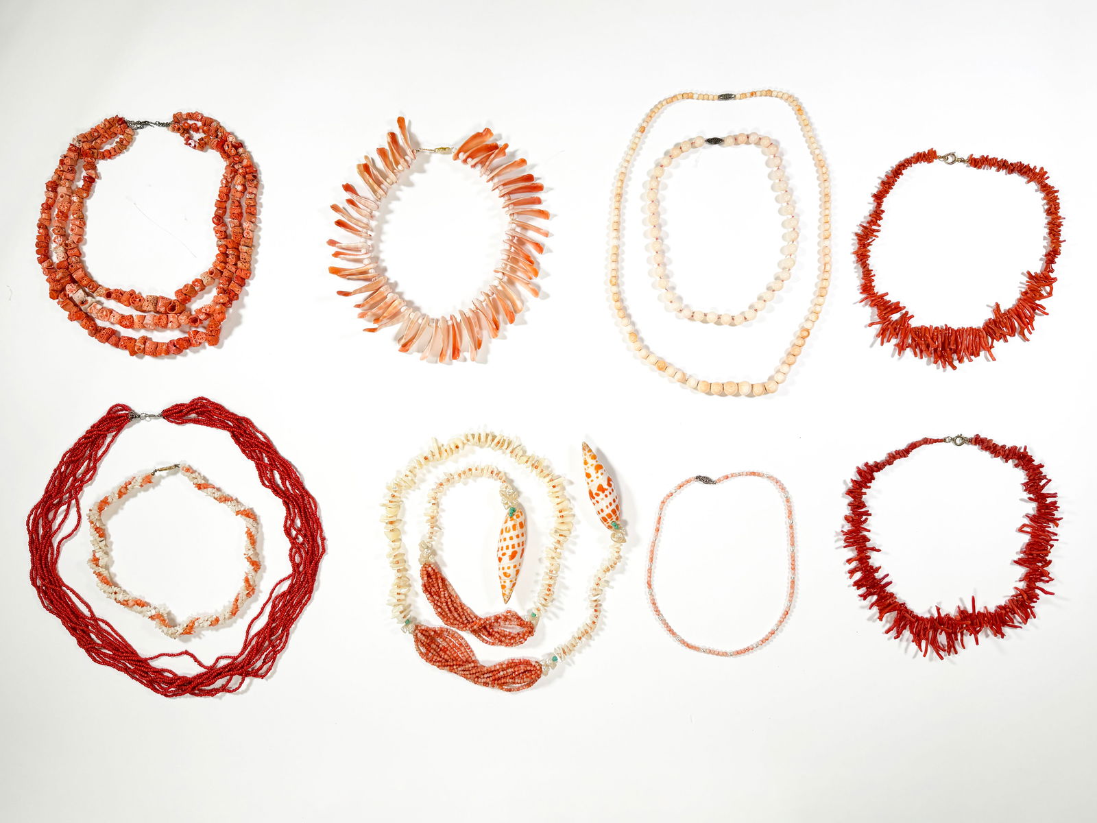 Collection of Coral and Shell Necklaces: A collection of necklaces featuring coral and shell beads. Includes various styles, bead sizes, and colors, ranging from deep red coral to light peach and white shells. Some necklaces have