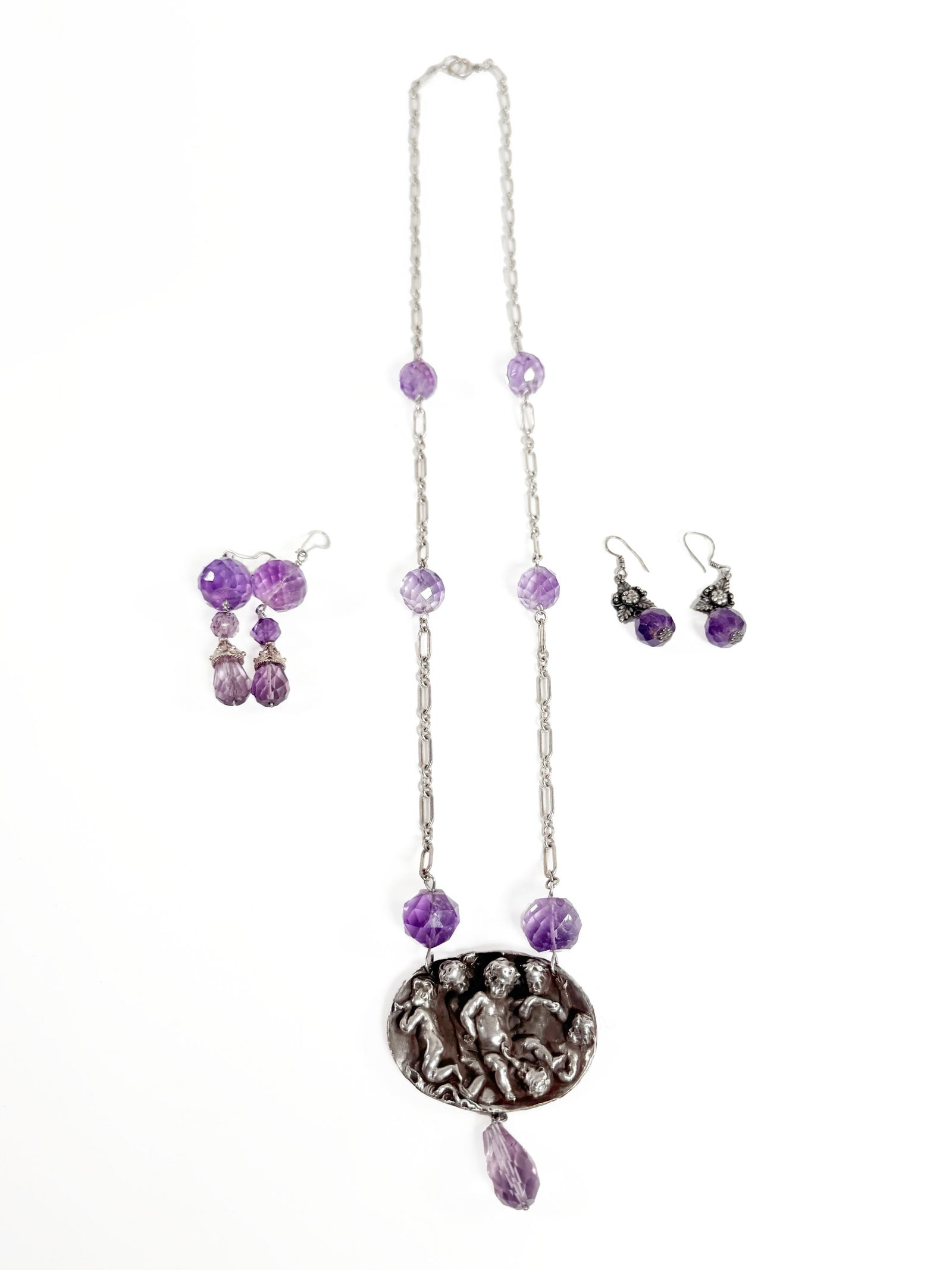 Sterling Silver Amethyst Necklace & Earring Set: Sterling silver necklace and earring set featuring amethyst beads. The necklace pendant depicts cherubs playing instruments. Includes two pairs of earrings, one marked "Kawi, 925." Necklace