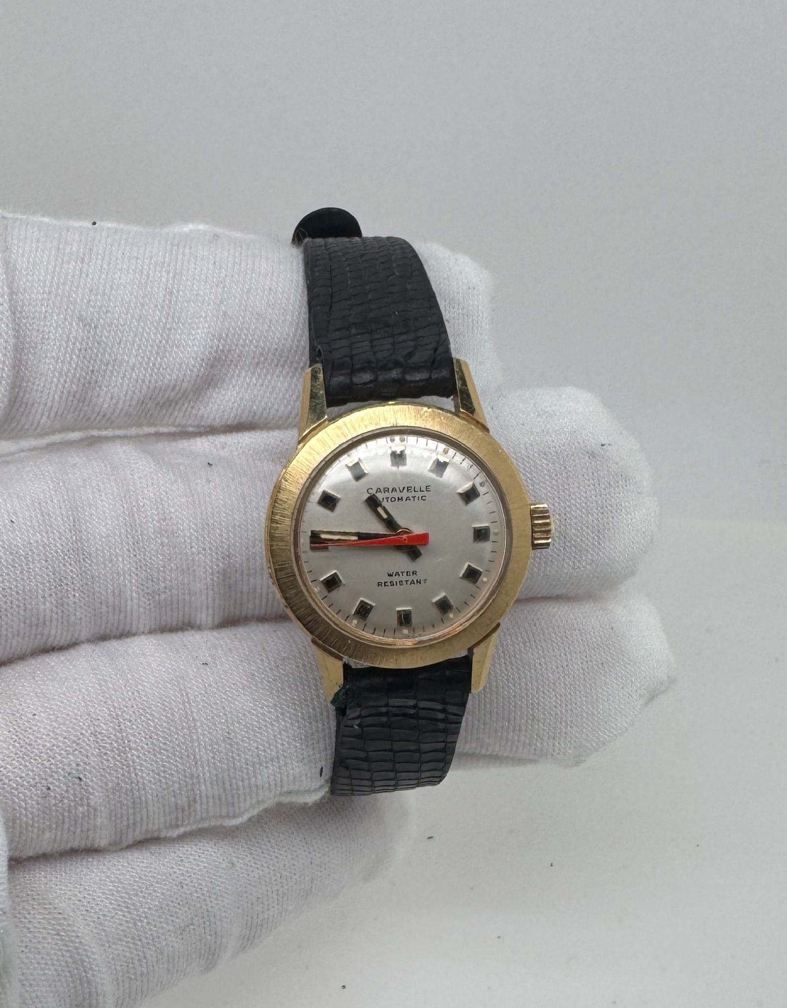 Caravelle Automatic Gold Plated Wristwatch, Ladies: Caravelle Automatic wristwatch with a gold-tone case and black leather strap. The watch features a silver dial with red second hand. The case back is marked with the number 3175. 17J Movement