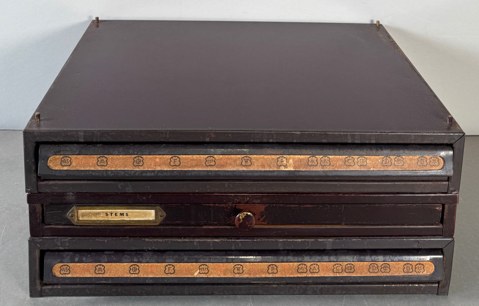 Vintage Three-Drawer Cabinet of assorted parts in glass vials (including stems): Three-drawer cabinet with decorative drawer fronts. full of glass vials containing watch parts. This includes a significant number of stems. Dimensions: 6 inches high x 13.25 inches wide.