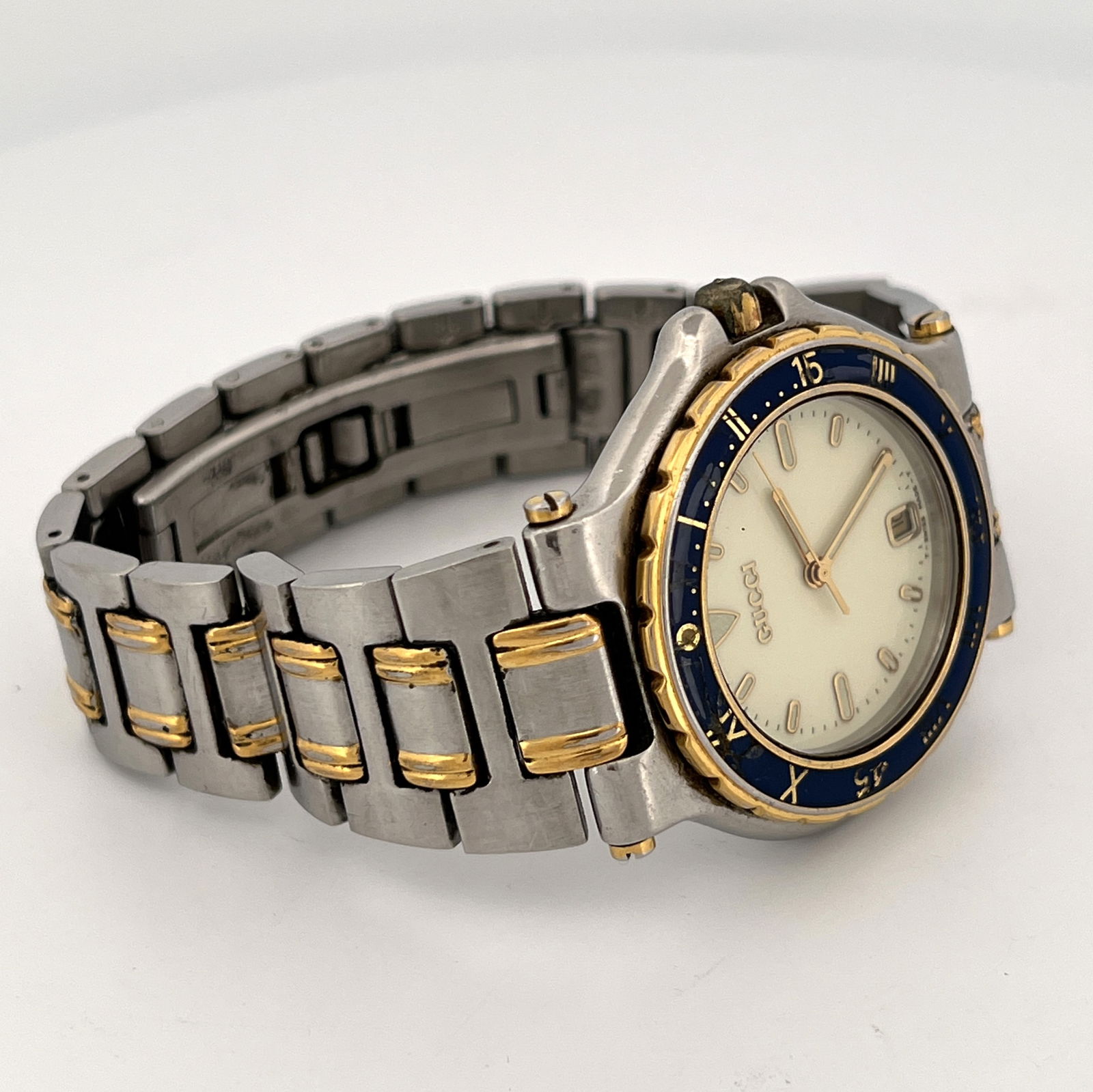Gucci 9700M Two-Tone Stainless Steel Wristwatch: Gucci Men's Dive Watch with a two-tone stainless steel case, two-tone integrated bracelet, blue and gold bezel, and date display at 6 o'clock. It features an ivory dial with a