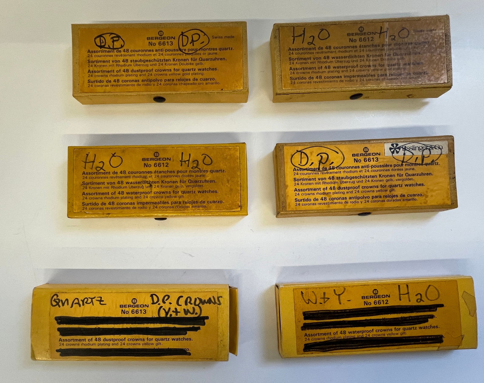 Bergeon Watch Crowns Assortment (6 Boxes): Collection of six boxes of Bergeon watch crowns. Each box contains an assortment of crowns for quartz watches, organized by size and type. Boxes are marked with Bergeon logo and reference numbers. A