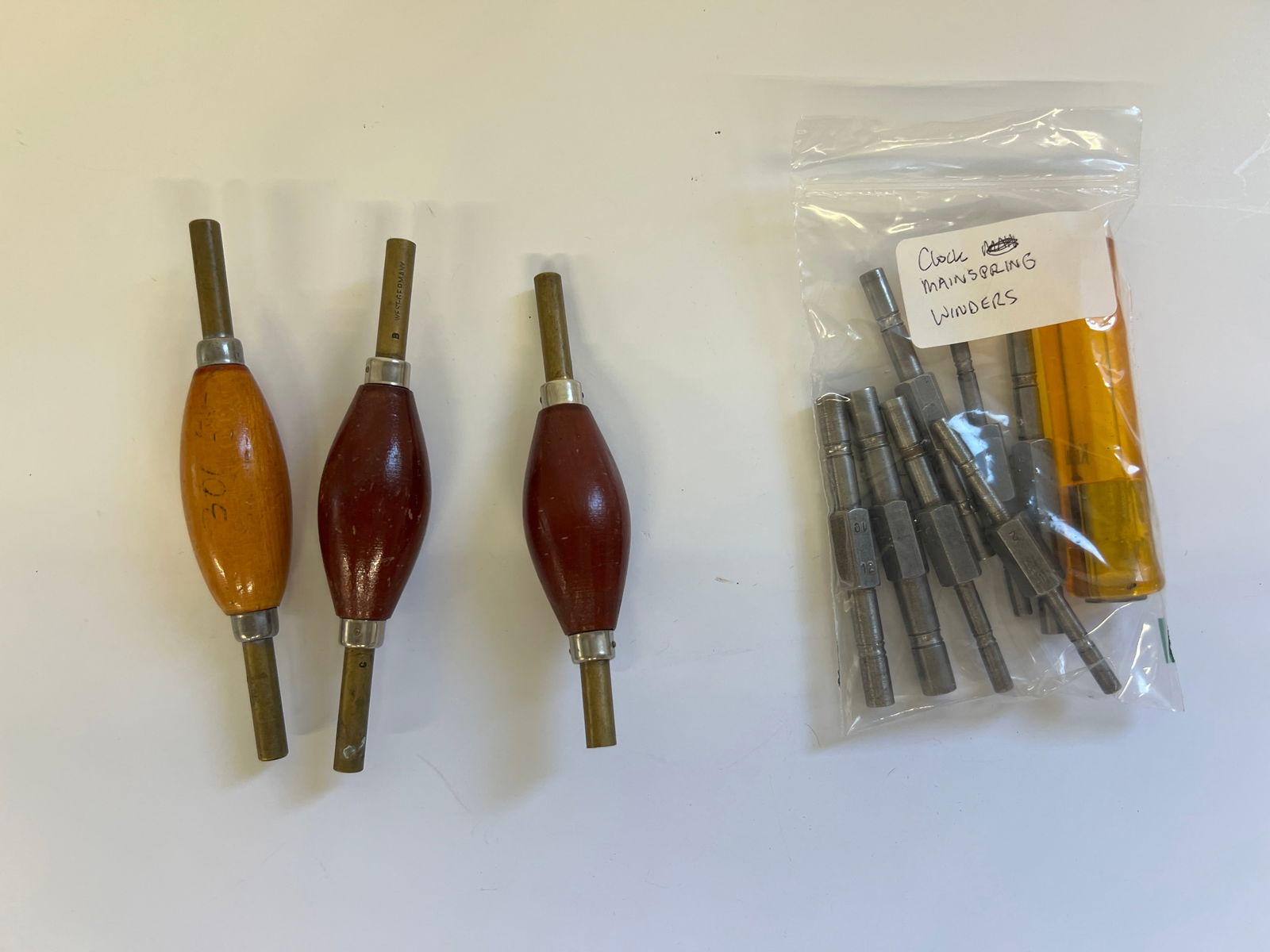 Clock Mainspring Let Down Tools- Group of Handles and Chucks: Collection of clock mainspring let down tools. Includes three winders with wooden handles and a bag of various sized chucks. Tools appear to be in good, usable condition.