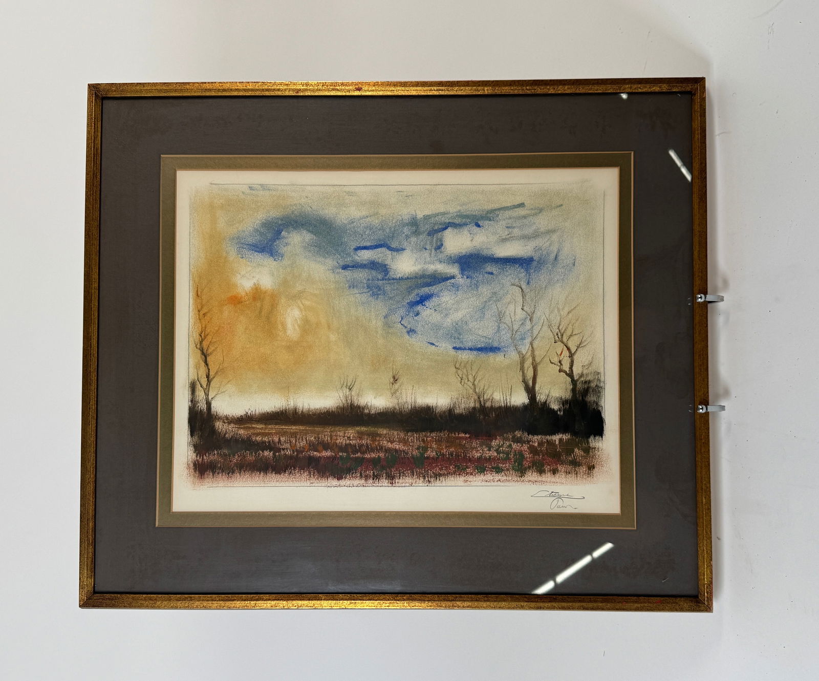 Framed Landscape Print: Framed landscape print featuring a field and trees under a cloudy sky. Matted and framed in a gold-tone frame. Frame dimensions: 19 x 22.5 inches. Print dimensions: 12.25 x 15.75 inches.