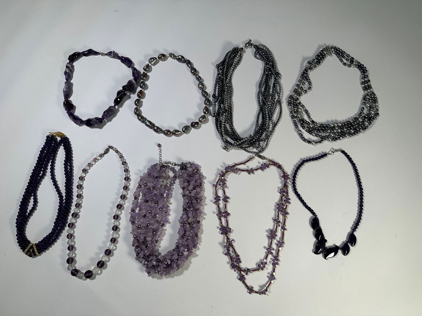 Group of Nine Fashion Necklaces: Collection of nine fashion necklaces featuring various bead types and colors, including purple and black. Four of the necklaces have sterling silver clasps. The longest necklace measures