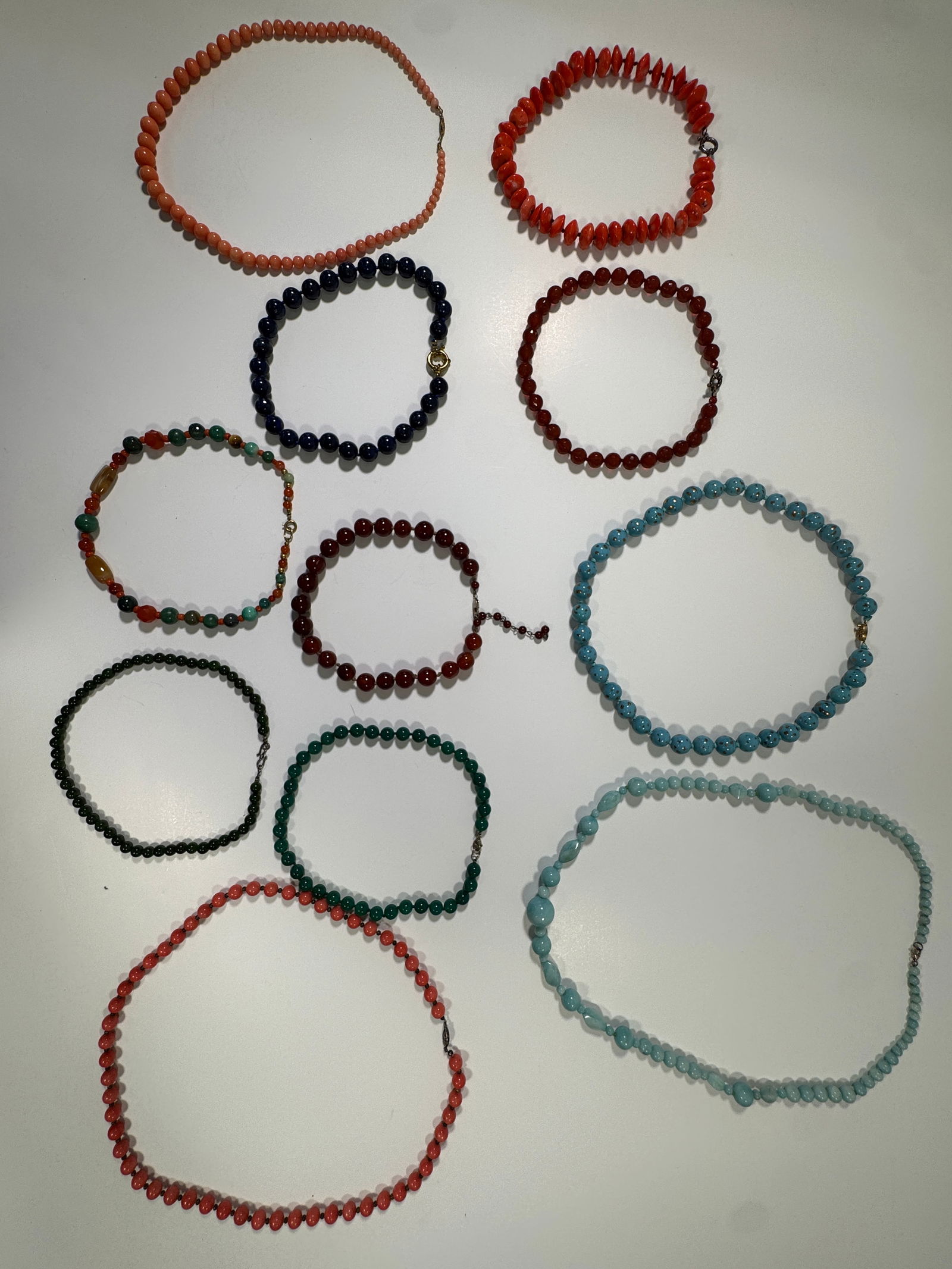 Collection of Beaded Necklaces: A collection of beaded necklaces featuring various colors and bead types. Includes coral, blue, green, and other colored beads. The necklaces have different lengths and clasp styles. Some of the