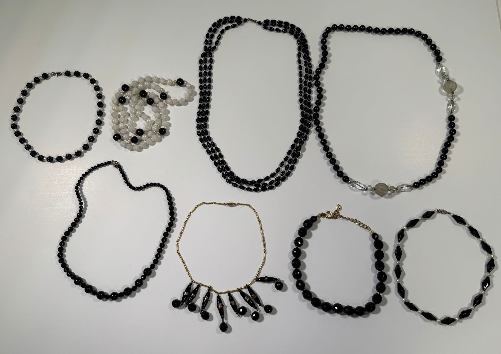 Collection of Vintage Beaded Necklaces: A collection of vintage beaded necklaces, featuring various styles and bead types. Includes black, white, and mixed bead designs with different lengths and clasps. Some necklaces feature unique