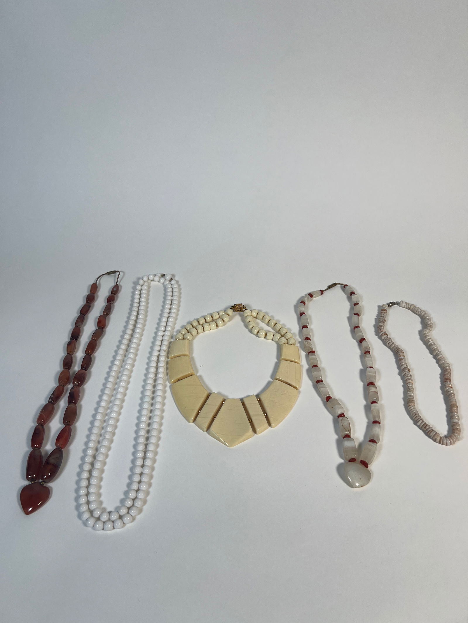 Collection of Costume Necklaces, Assorted Materials: A collection of six costume necklaces featuring various bead types and materials. Includes strands of white beads, brown beads, and unique geometric designs. Suitable for costume or fashion