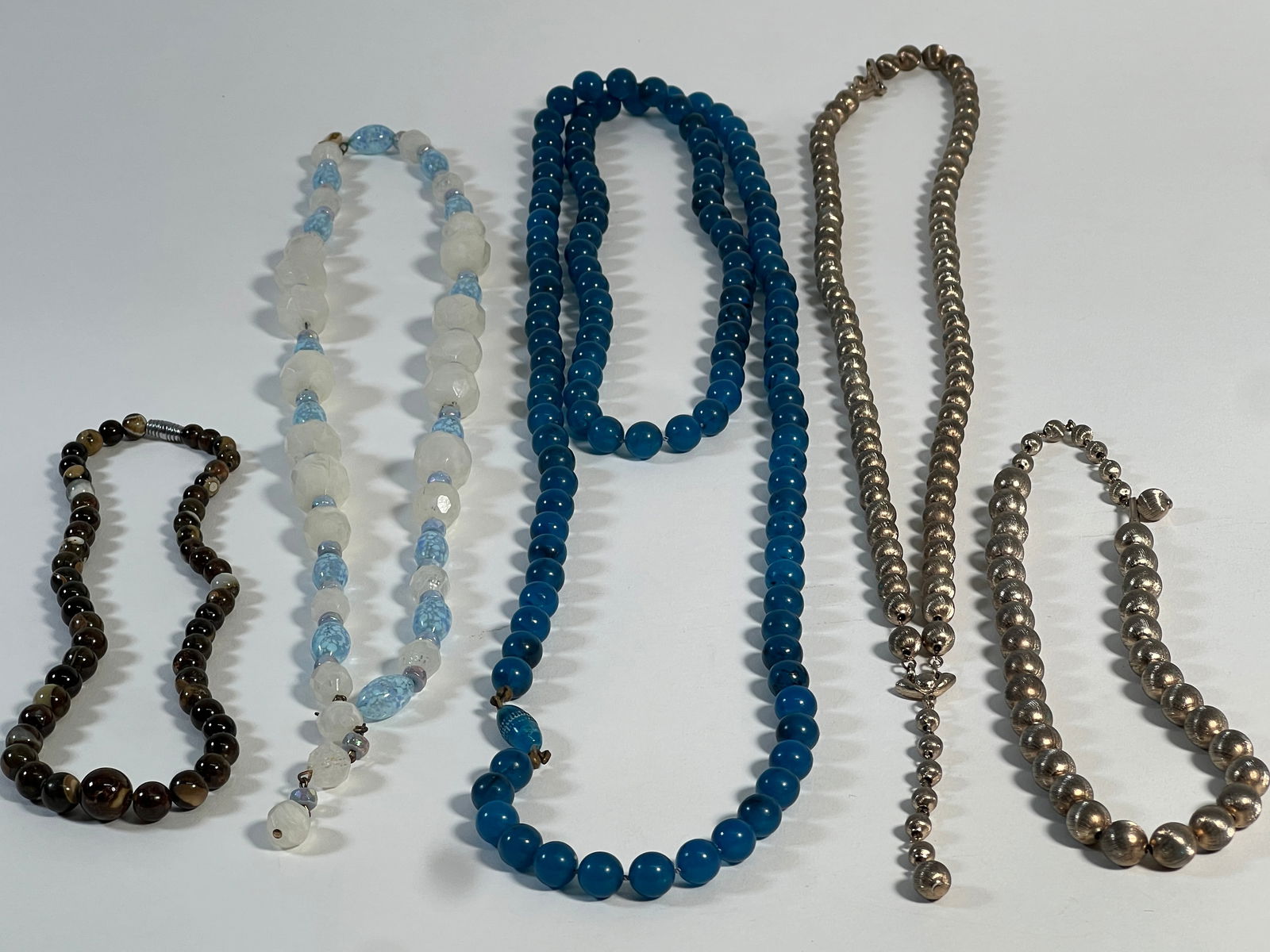 Group of Five Costume Necklaces: A collection of five costume necklaces featuring various bead types and colors, including silver tone, blue, white, and brown. Lengths vary.