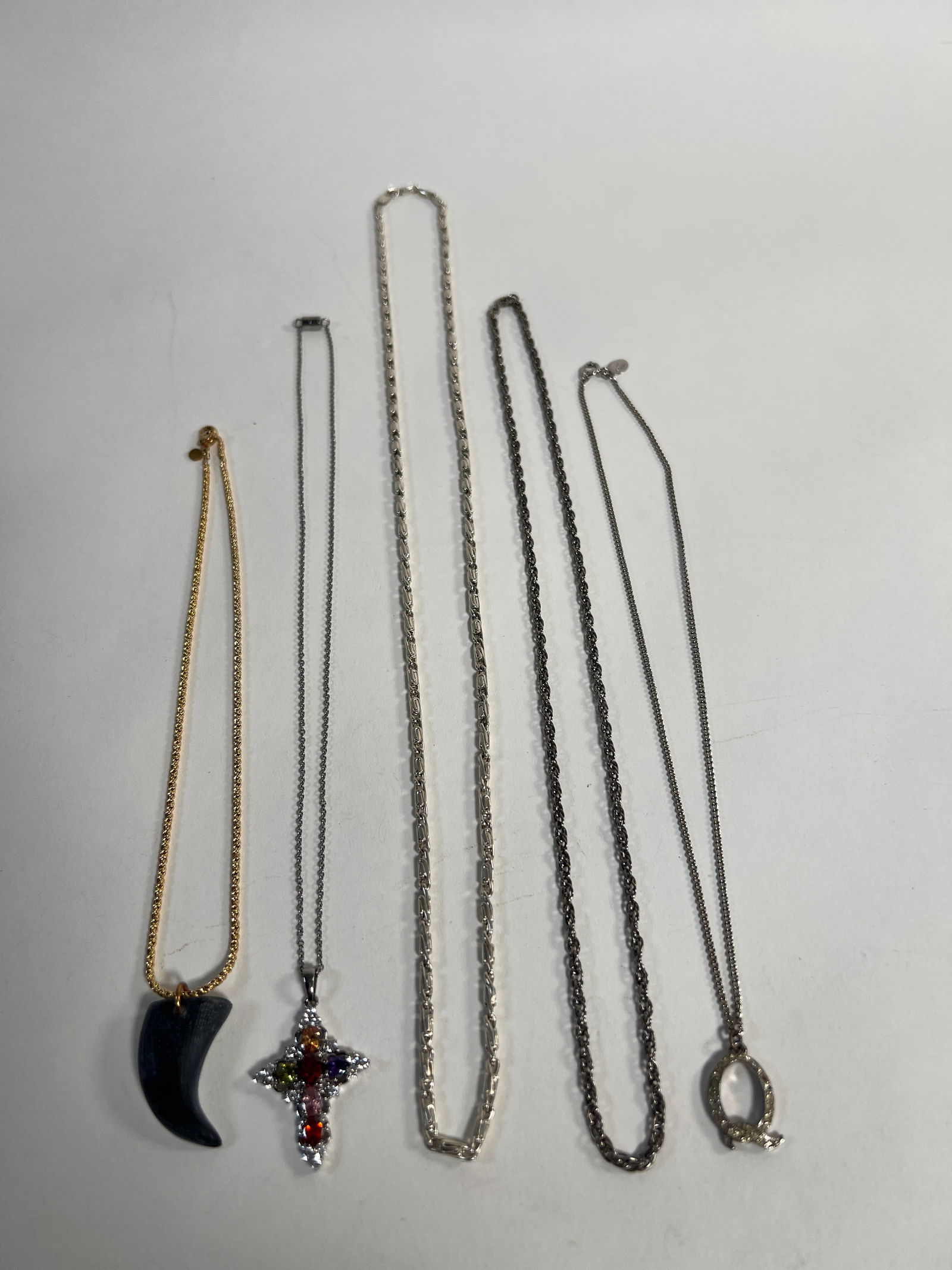 Group of Costume Necklaces: A collection of six costume necklaces featuring various chain styles and pendants, including a cross with colored stones and a black horn-shaped pendant. Lengths vary. Lengths : 15" to 9"