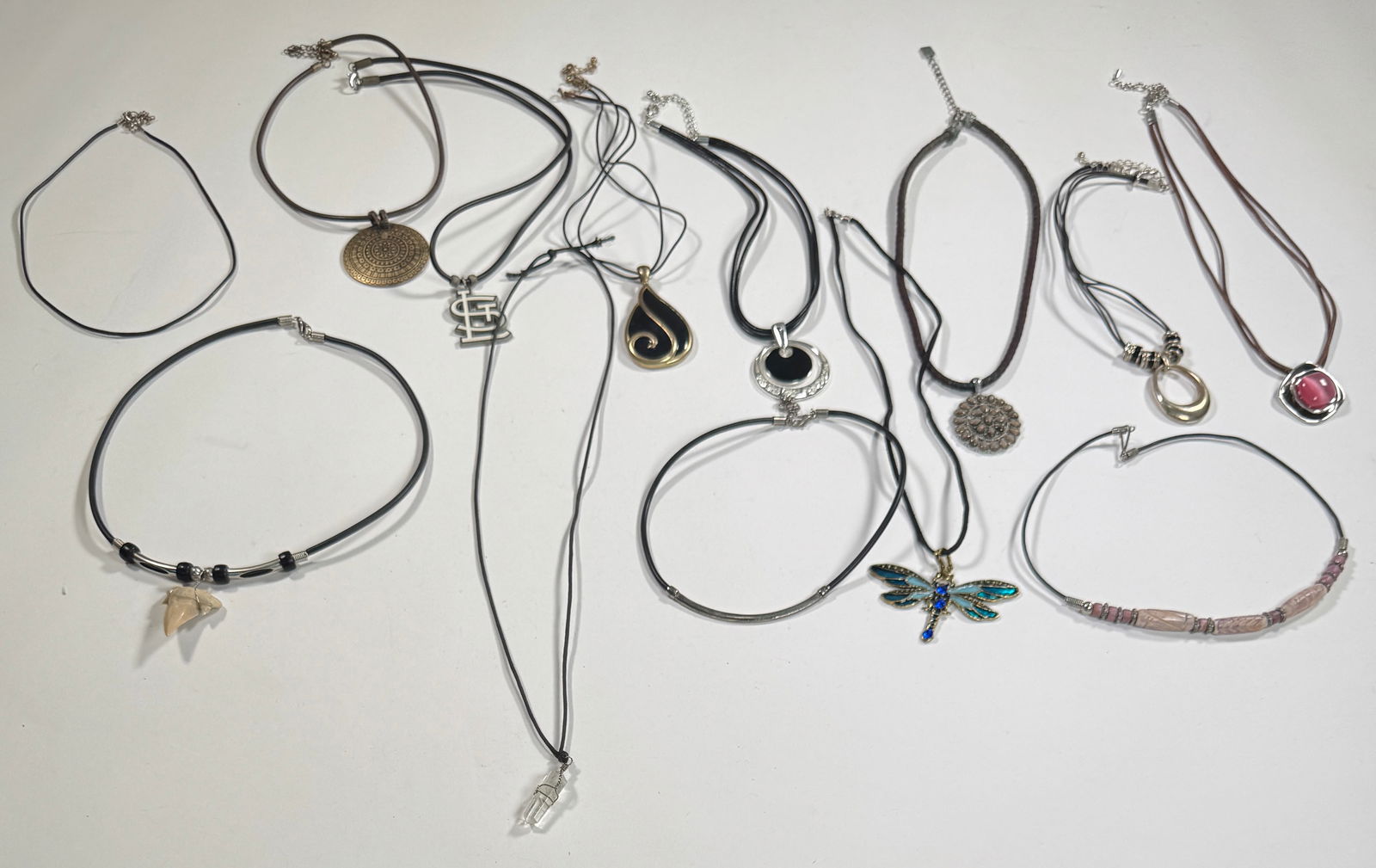 Group of Costume Necklaces: Collection of costume necklaces featuring various pendants on cords. Includes a shark tooth, dragonfly, and stone pendants. Longest necklace measures 13.5 inches. Total weight: 7 oz.
