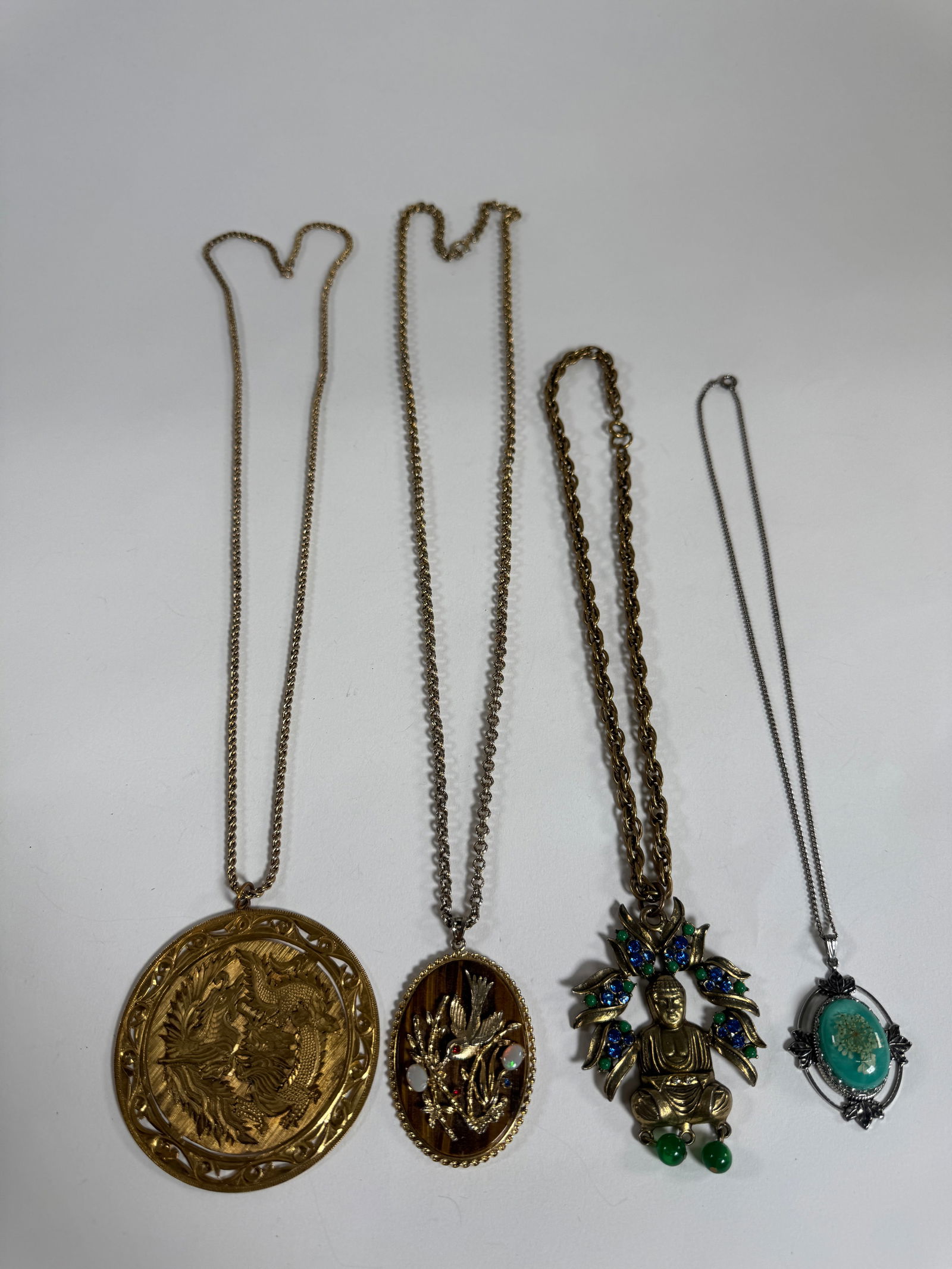 Group of Four Costume Necklaces: A group of four costume necklaces featuring various pendants, including a turquoise-colored stone, a Buddha figure with rhinestones, and two Asian-inspired designs. Longest necklace approximately 17