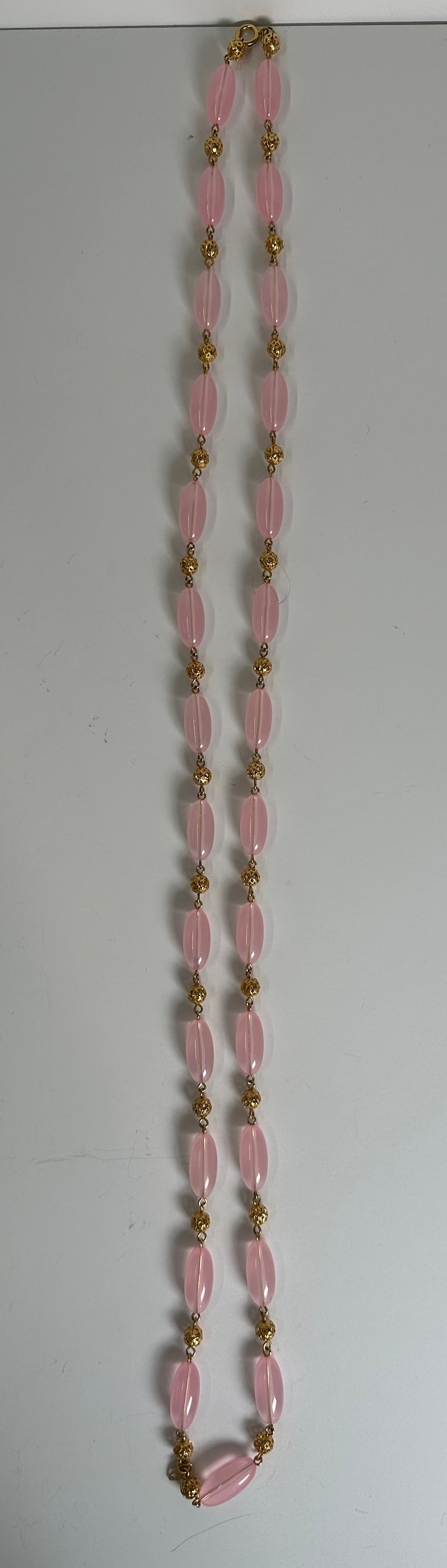 Pink Bead Necklace: A pink bead necklace with gold-tone accents. The necklace features oval-shaped pink beads separated by smaller gold-tone beads.