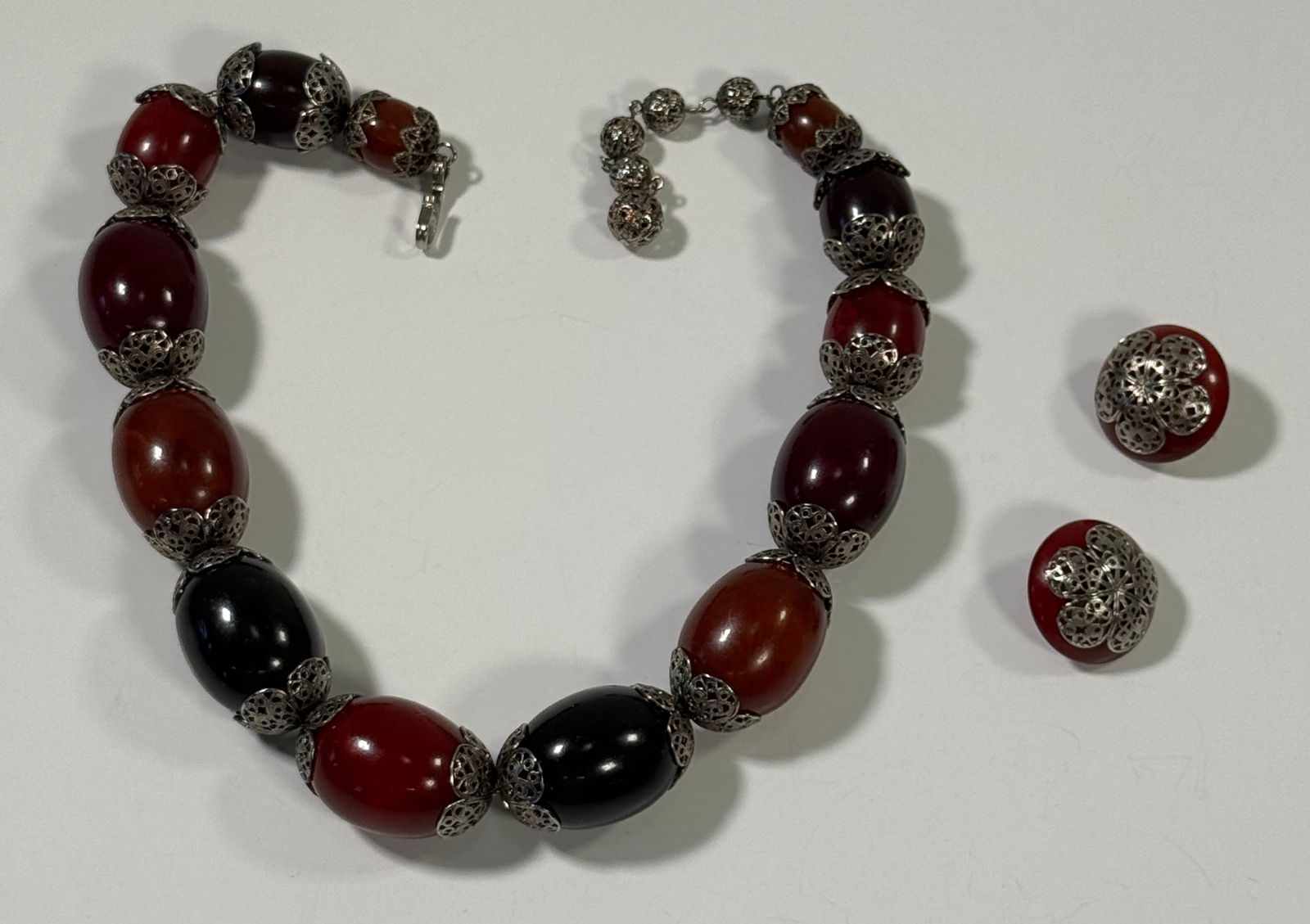 Vintage Bead Necklace and Earring Set: Vintage necklace and earring set featuring oval beads in shades of red, brown, and black, separated by ornate silver-tone caps. The earrings are round with matching silver-tone filigree. Length : 19&q