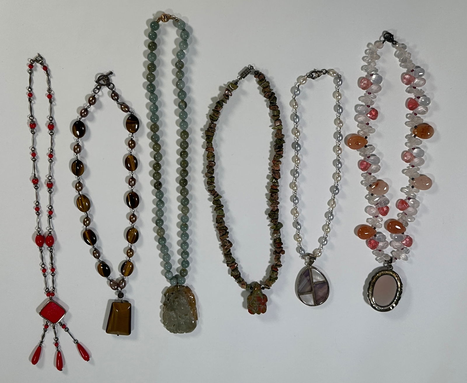Group of Six Beaded Necklaces with Pendants: This lot features six beaded necklaces, each with a unique pendant. The necklaces showcase a variety of bead types and colors, including red, brown, green, and pink. Pendants include carved stones and