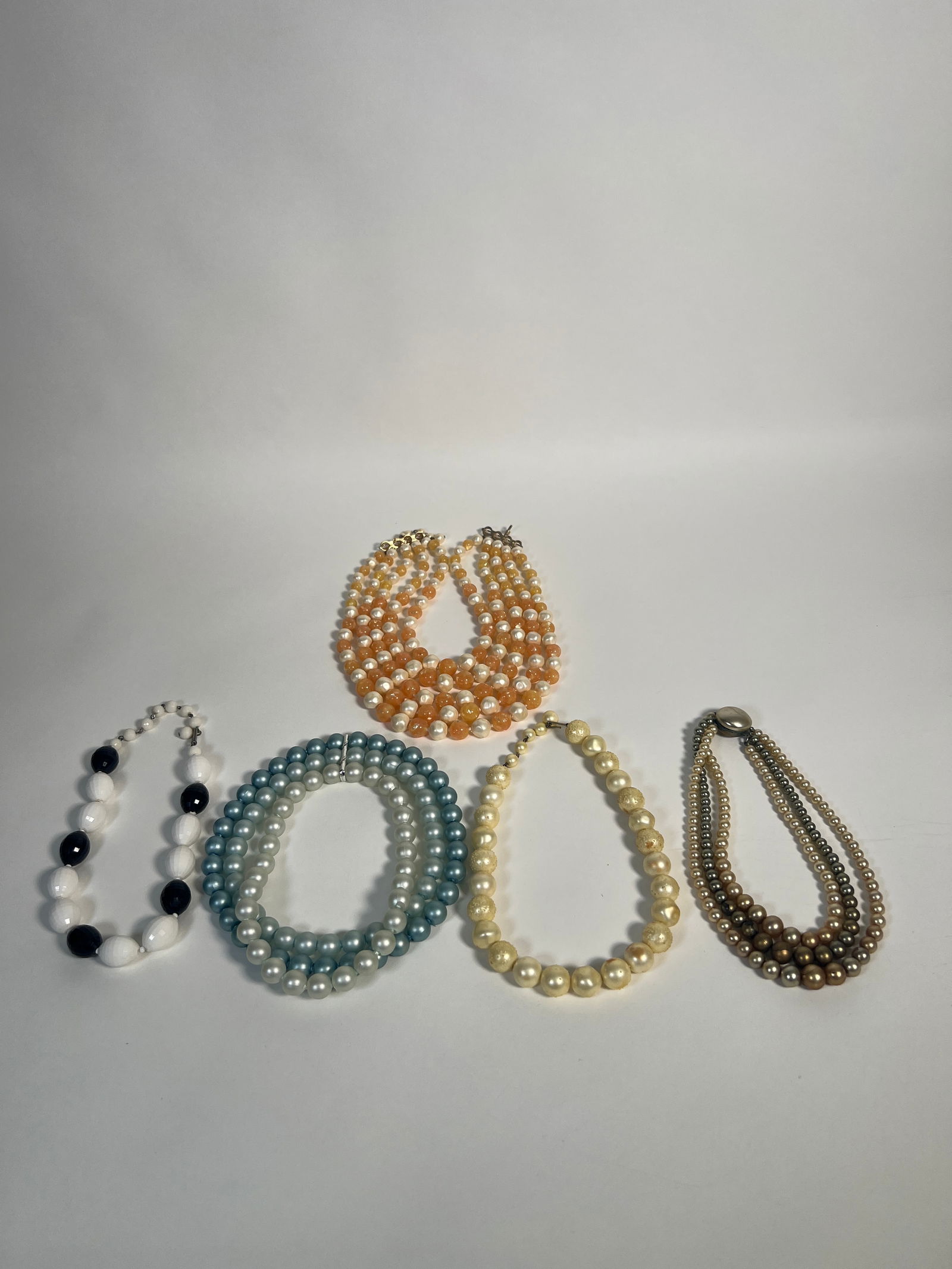 Costume Jewelry: Five Beaded Bracelets: A collection of five beaded bracelets. Includes multi-strand faux pearl bracelets in various colors, including brown, cream, and blue. One bracelet features alternating black and white beads. Costume