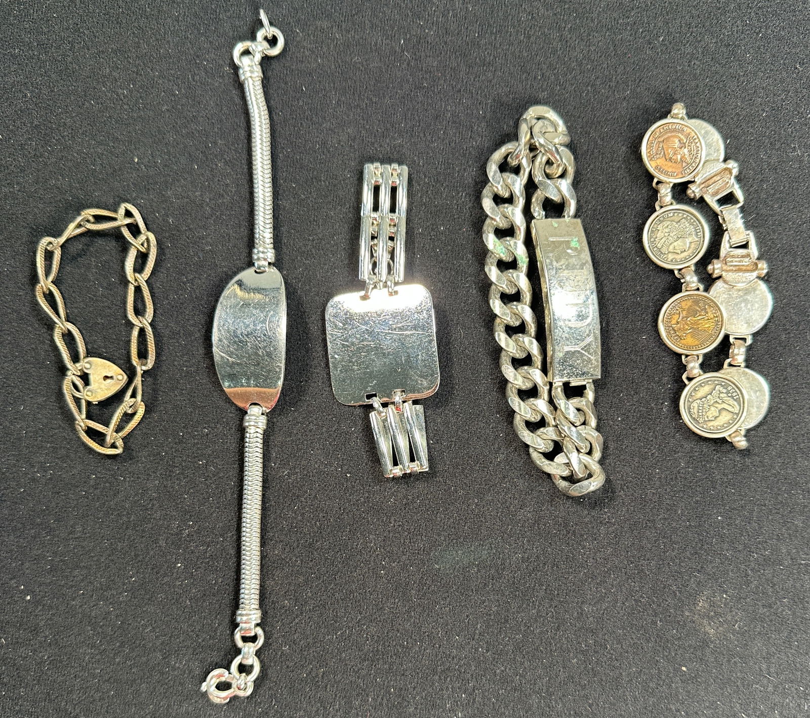 Five Silver Tone Metal and Sterling Bracelets: Collection of five silver tone metal bracelets, including coin bracelet, chain bracelet, and ID bracelet. Bracelet with coins is sterling silver. Various designs and closures. See images for details.