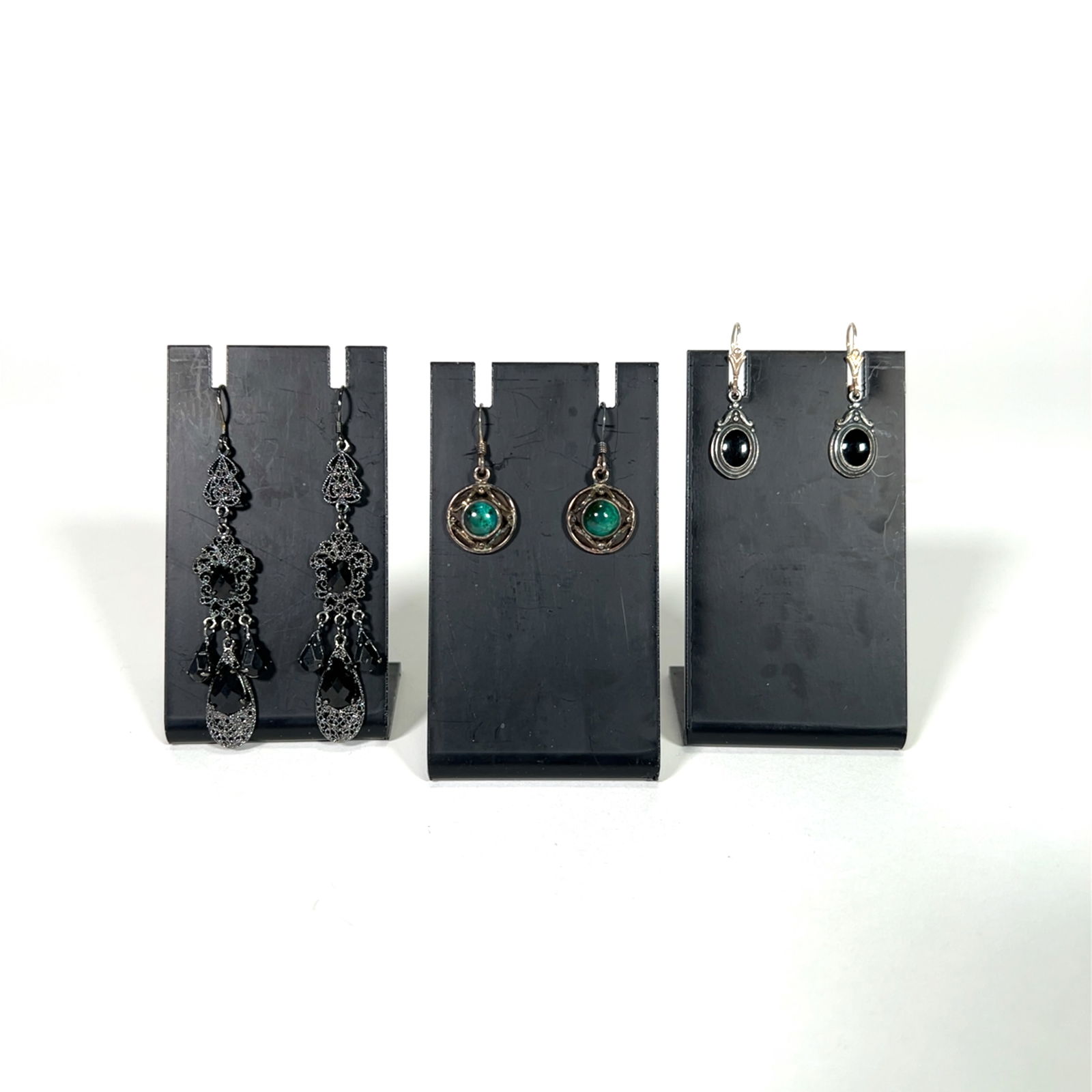 Three Pairs of Earrings: Includes three pairs of earrings. Two pairs are marked sterling silver. One pair features black stones, another green stones, and the third is a long, dangling pair with black accents.
