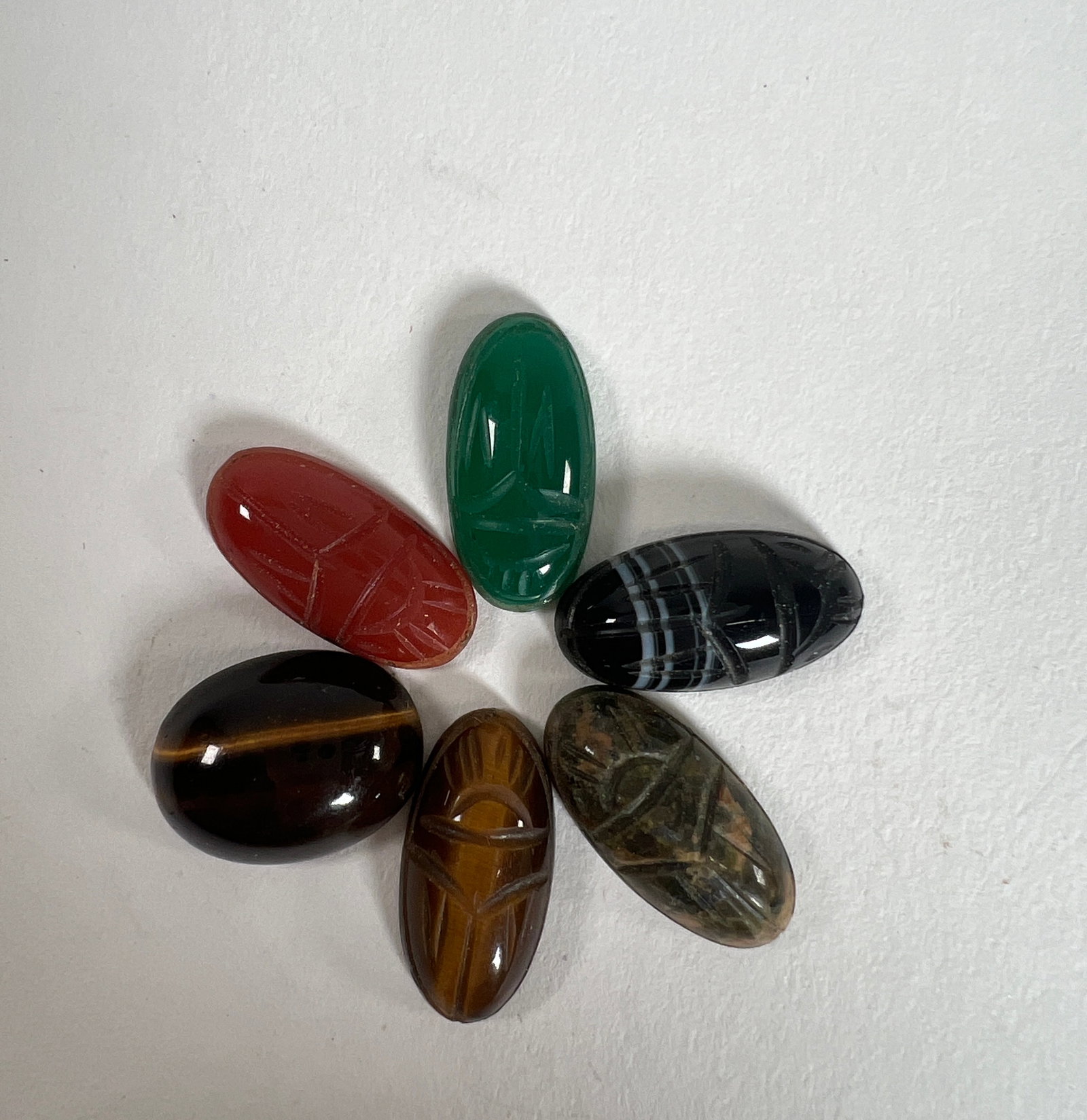 Group of Six Carved Stone Scarabs: This lot features six carved stone scarabs in various colors and patterns. The stones include tiger's eye, banded agate, carnelian, and green onyx. Each scarab is carved with details. Weight: 0.3