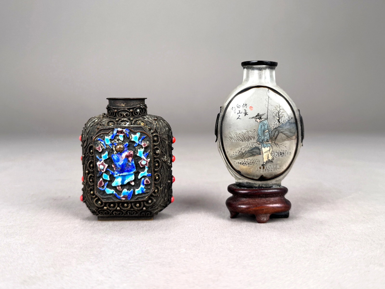 Two Chinese Snuff Bottles: A group of two Chinese Snuff Bottles. Includes one metal filigree bottle with enamel and coral inserts and a glass bottle with a reverse painted scene of a man in the mountains. The glass bottle