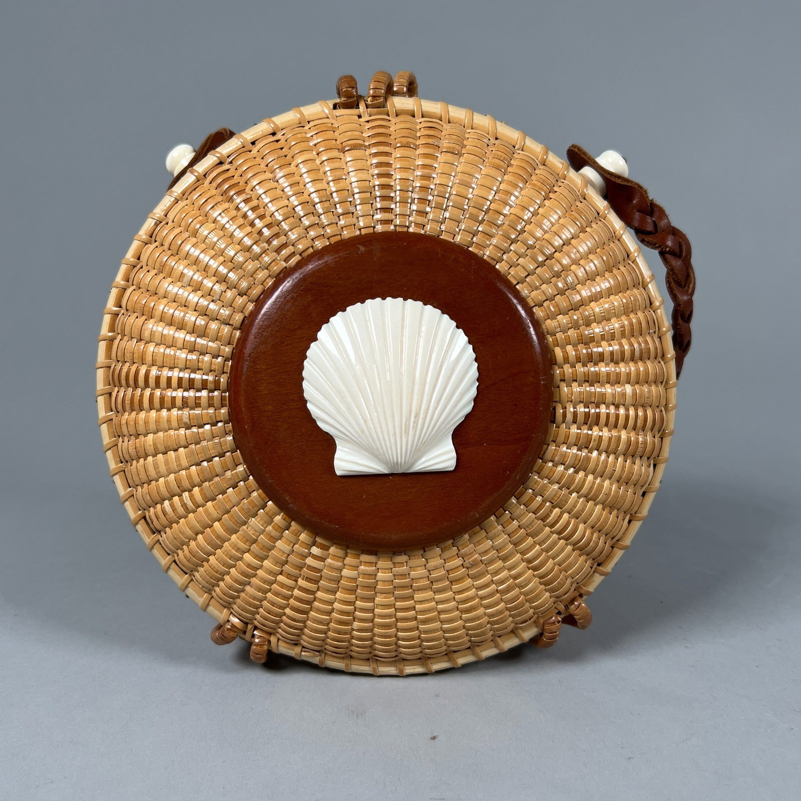 Nantucket Lightship Basket Purse with Scallop Detail: A Nantucket Lightship basket/purse with a nameplate on the interior and a caved scallop on the top. Features a leather crossbody strap and a lined fabric interior with a pocket. Strap length: