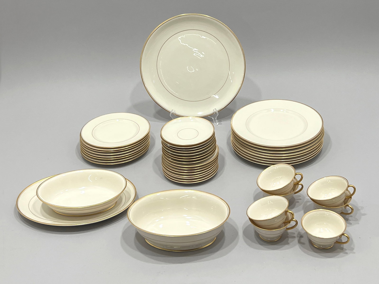 Set of Franciscan China with Gold Trim: A vintage set of Fraciscan china featuring a cream-colored glaze with a delicate gold trim. The set includes dinner plates, salad plates, bowls, and cups and saucers. Each piece is stamped on the