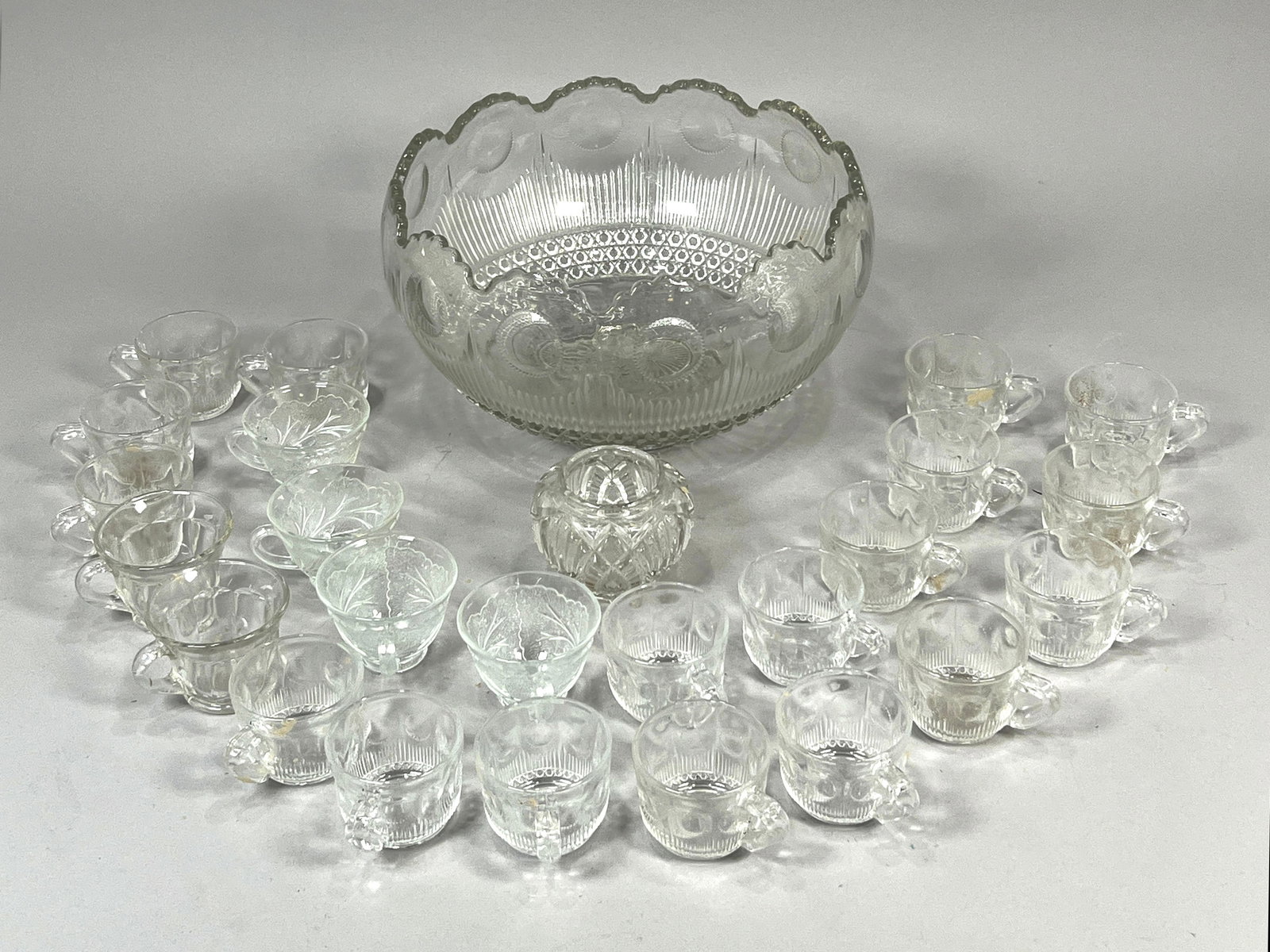 Group of Glass Punch Glasses and Bowl: A scalloped edge punch bowl with intricate detailing and matching glass cups. The bowl measures 13 inches in width and the set weighs 21lb 14oz.
