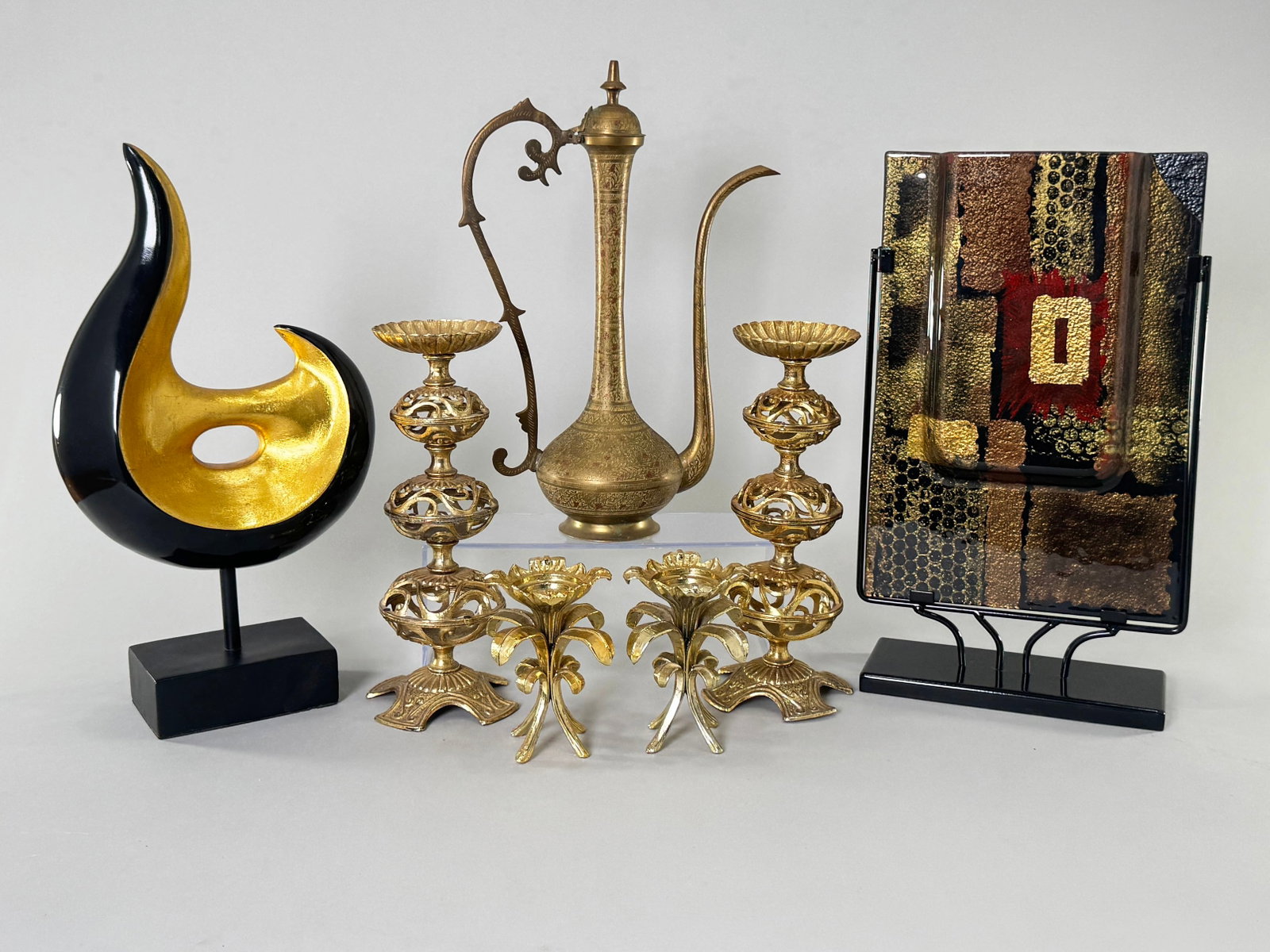 Mixed Decorative Arts Lot: Sculpture, Candlesticks, Pitcher, Art Glass: A mixed lot of decorative arts including a black and gold sculpture, four gold-tone candlesticks, a brass pitcher with etched designs, and a piece of art glass on a stand. Largest item measures 17.5 i