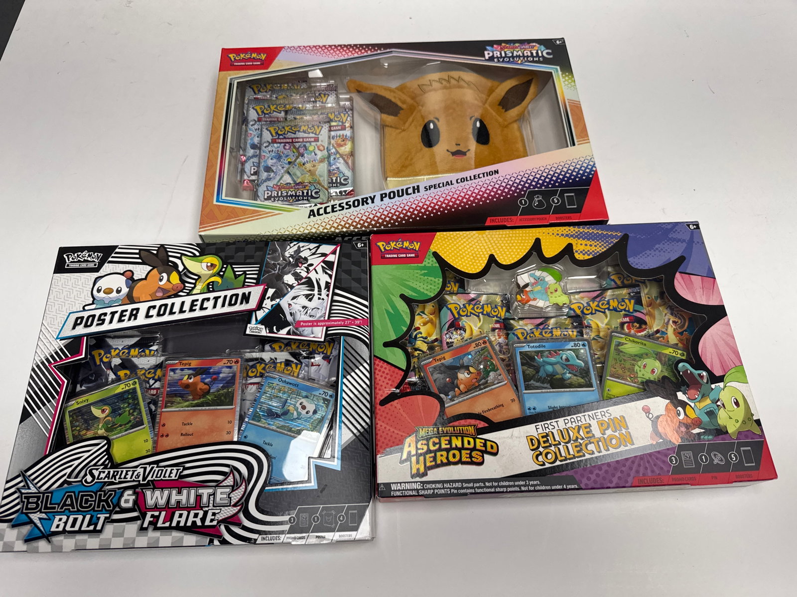 Pokemon TCG Accessory Pouch, Poster, and Deluxe Pin Collection Boxes: This lot includes three Pokemon Trading Card Game (TCG) collection boxes: the Prismatic Evolutions Accessory Pouch Special Collection featuring Eevee, the Scarlet & Violet Black & White Flare Poster C
