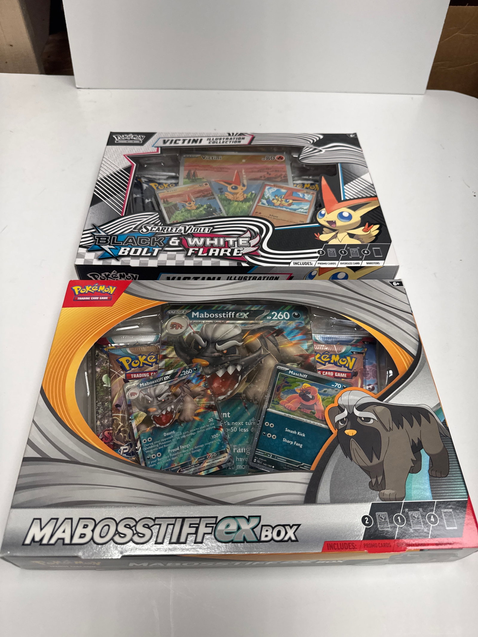 Pokemon TCG: Victini Illustration Collection & Mabosstiff EX Box: This lot includes two Pokemon Trading Card Game (TCG) boxes: the Victini Illustration Collection and the Mabosstiff EX Box. The Victini box features a full-art promo card of Victini, two Pokemon TCG b