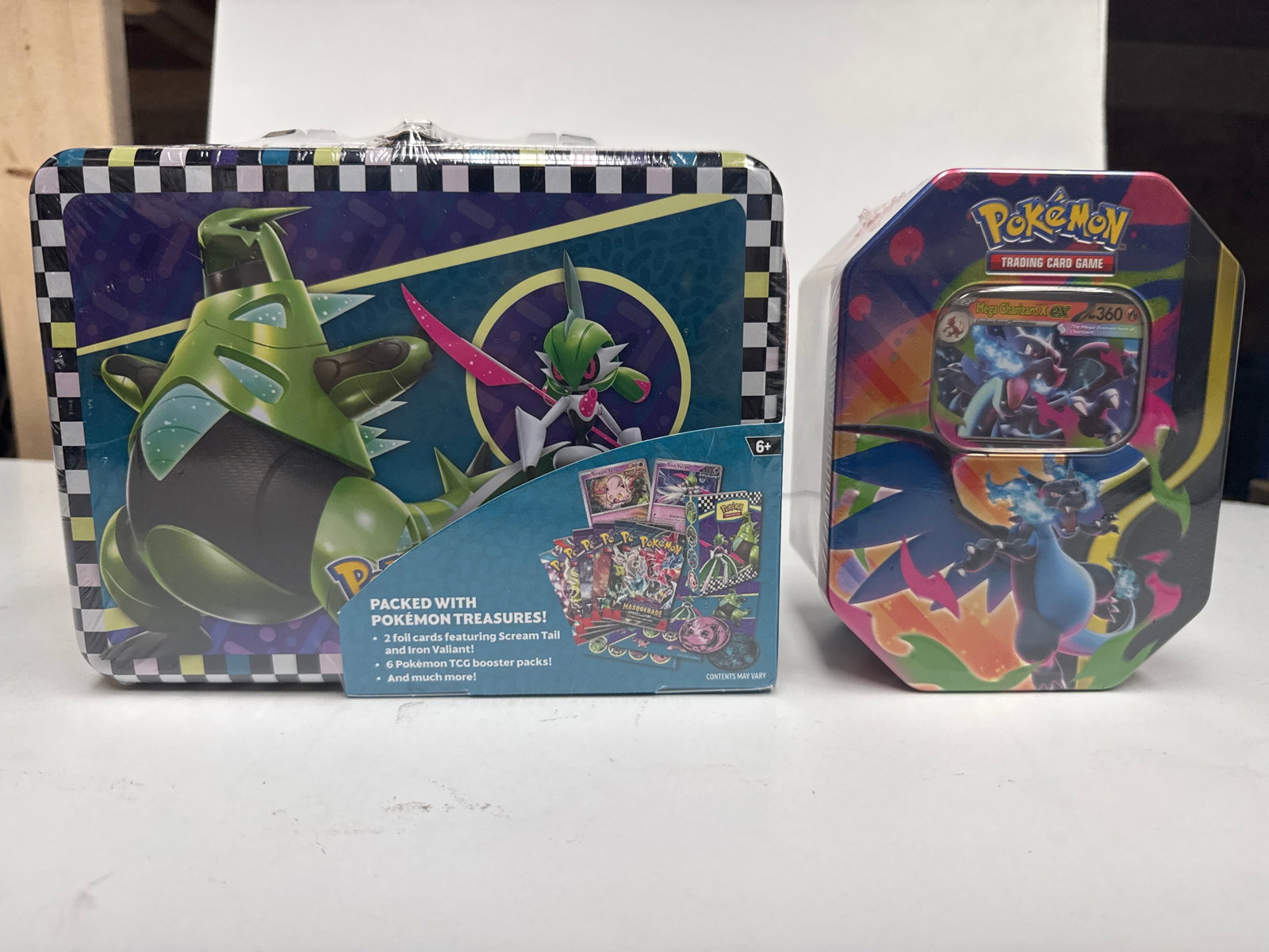 Pokemon Trading Card Game Collector's Chest Tin/Luncbox: This lot includes two sealed Pokemon Trading Card Game collector's tins. The larger tin is a metal lunchbox featuring various Pokemon, and the smaller tin is octagonal and features Mega Charizard EX. 