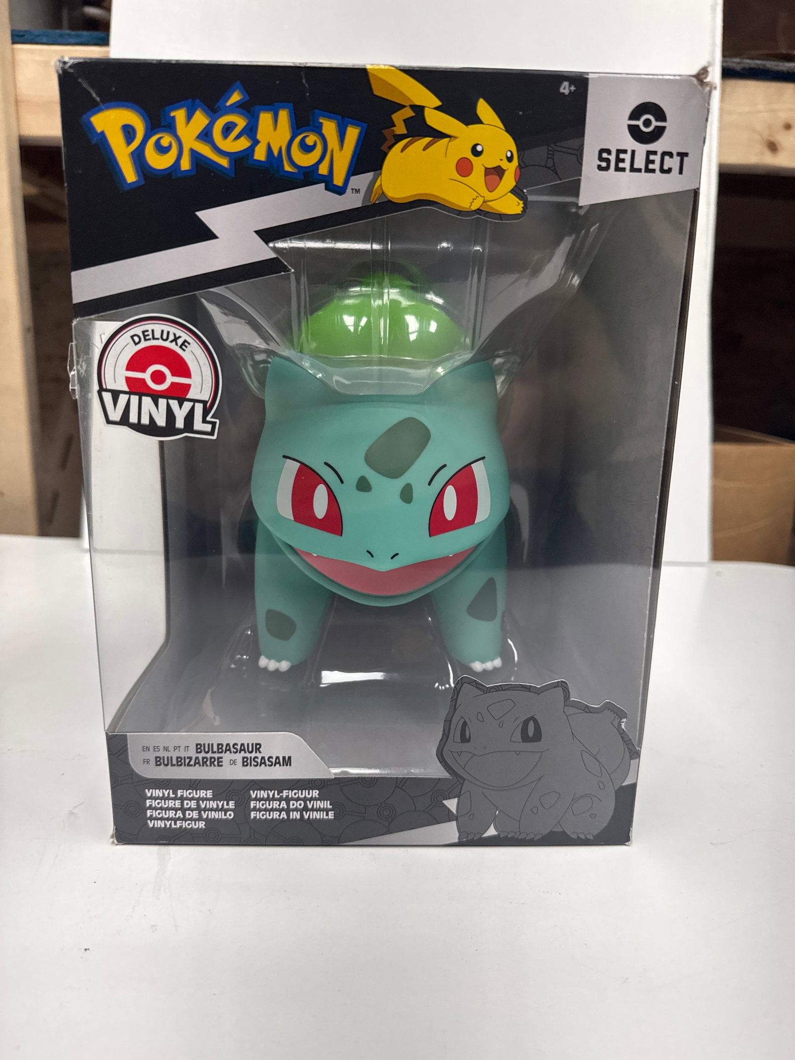 Pokemon Select Deluxe Vinyl Bulbasaur Figure: A brand new, unopened Pokemon Select Deluxe Vinyl figure featuring Bulbasaur. This collectible item is part of Series 2 and is suitable for ages 4 and up. The packaging shows the iconic Pokemon logo a
