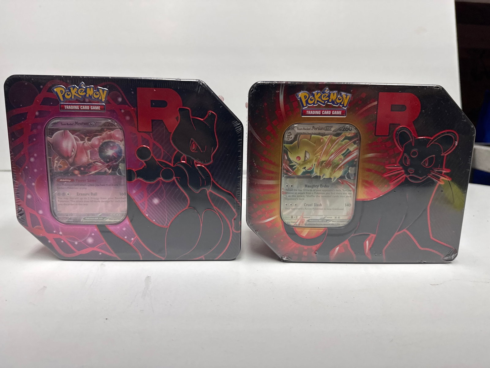 Pokemon Trading Card Game Team Rocket Tins - Mewtwo EX and Persian EX: This lot features two Pokemon Trading Card Game tins, each showcasing a powerful Pokemon EX card. The left tin features Team Rocket's Mewtwo EX with its 'Power Saver' ability and 'Erasure Ball' attack