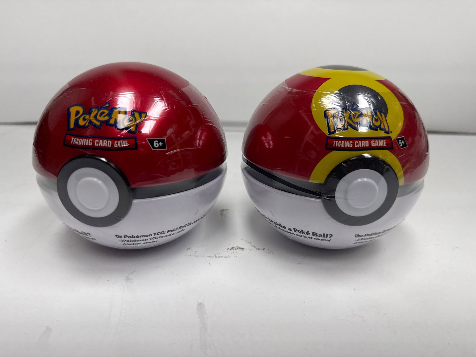 Two Pokemon Trading Card Game Poke Ball Tins: This lot includes two Pokemon Trading Card Game Poke Ball tins. Each tin contains Pokemon TCG booster packs and sticker sheets. Recommended for ages 6+.